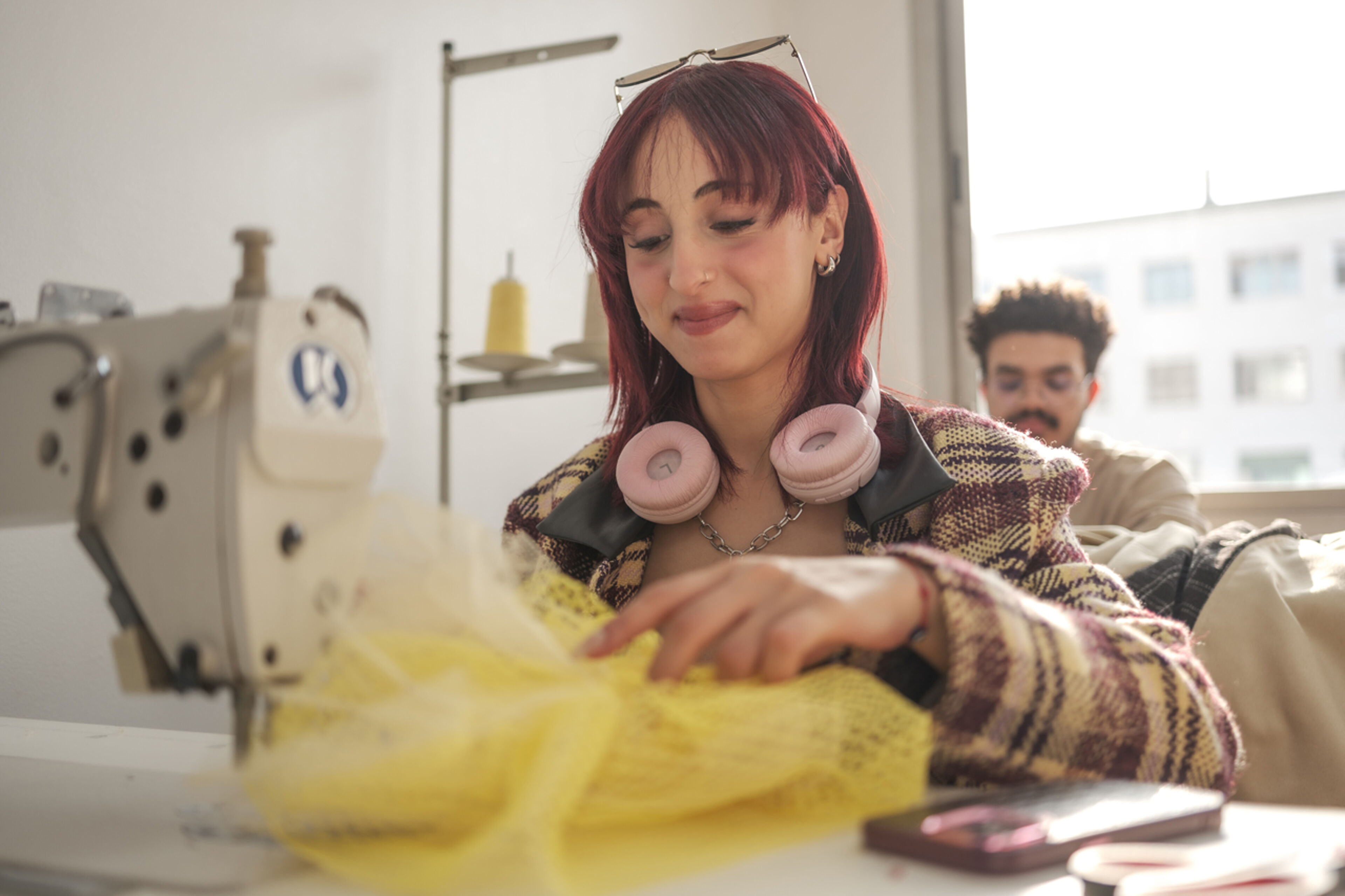 A focused seamstress with red hair sews yellow fabric on an industrial sewing machine.