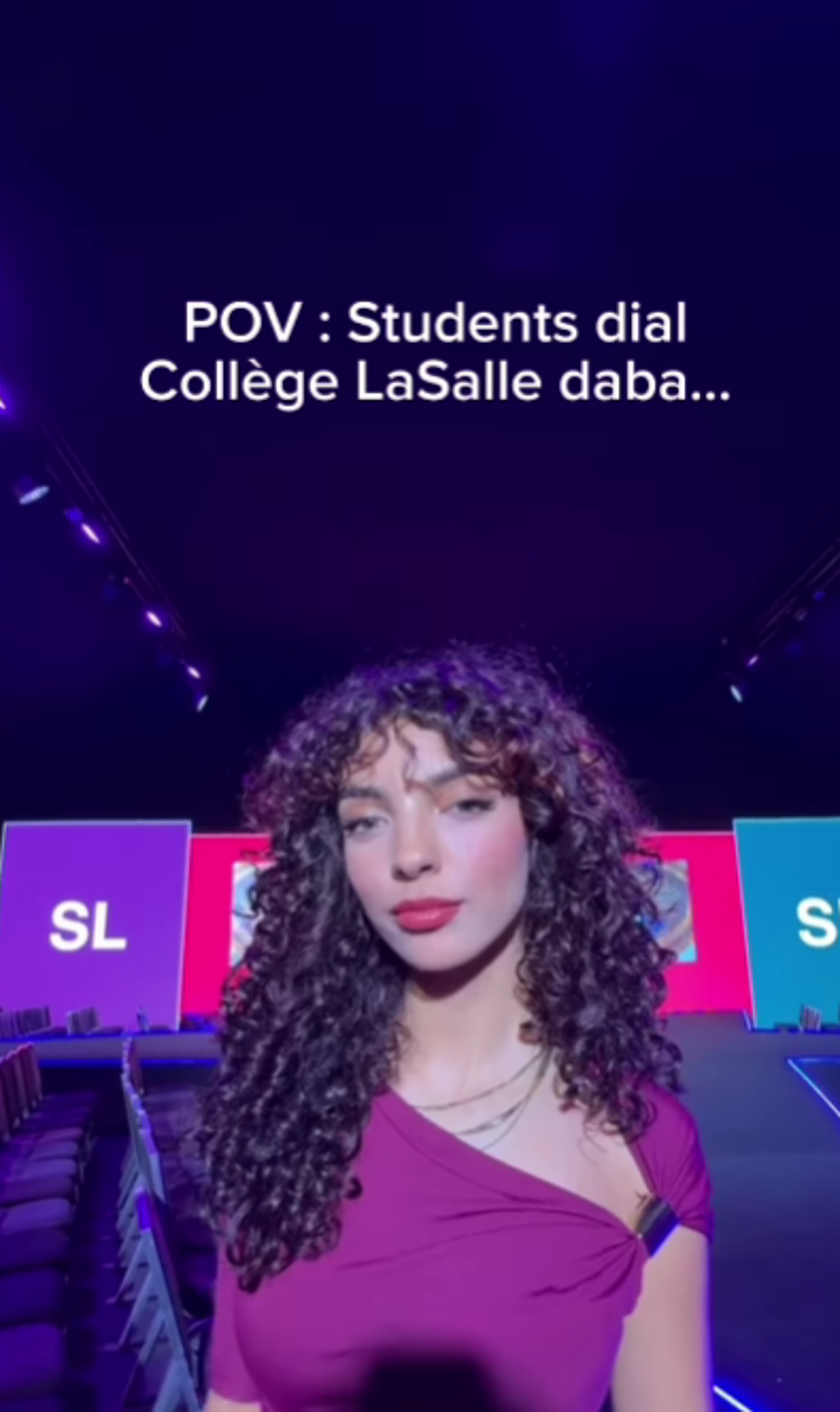 A young woman with curly hair and red lipstick stands in front of a stage with the words 'Collège LaSalle' visible. She is wearing a purple dress with one shoulder exposed. The background is a vibrant purple and blue, suggesting a formal event or presentation.