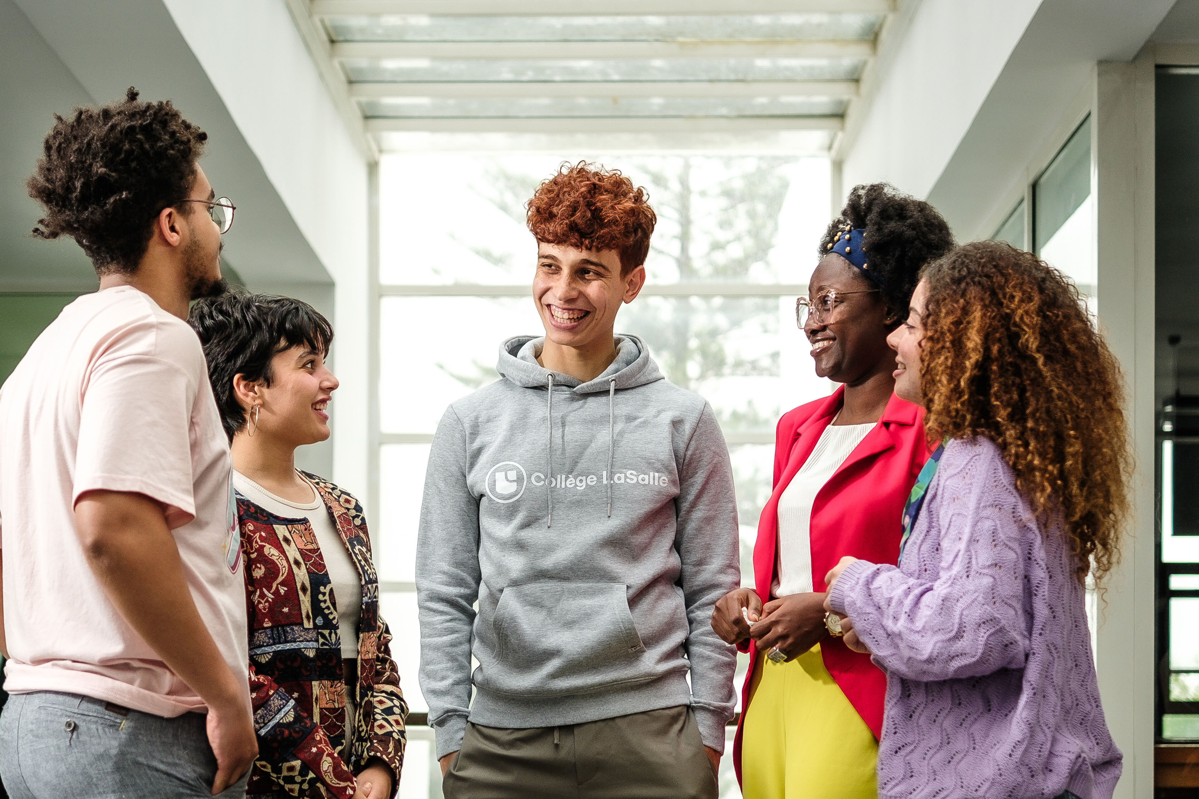 Five young adults in casual attire share a joyful conversation in a brightly lit indoor space, reflecting a lively and inclusive academic environment.