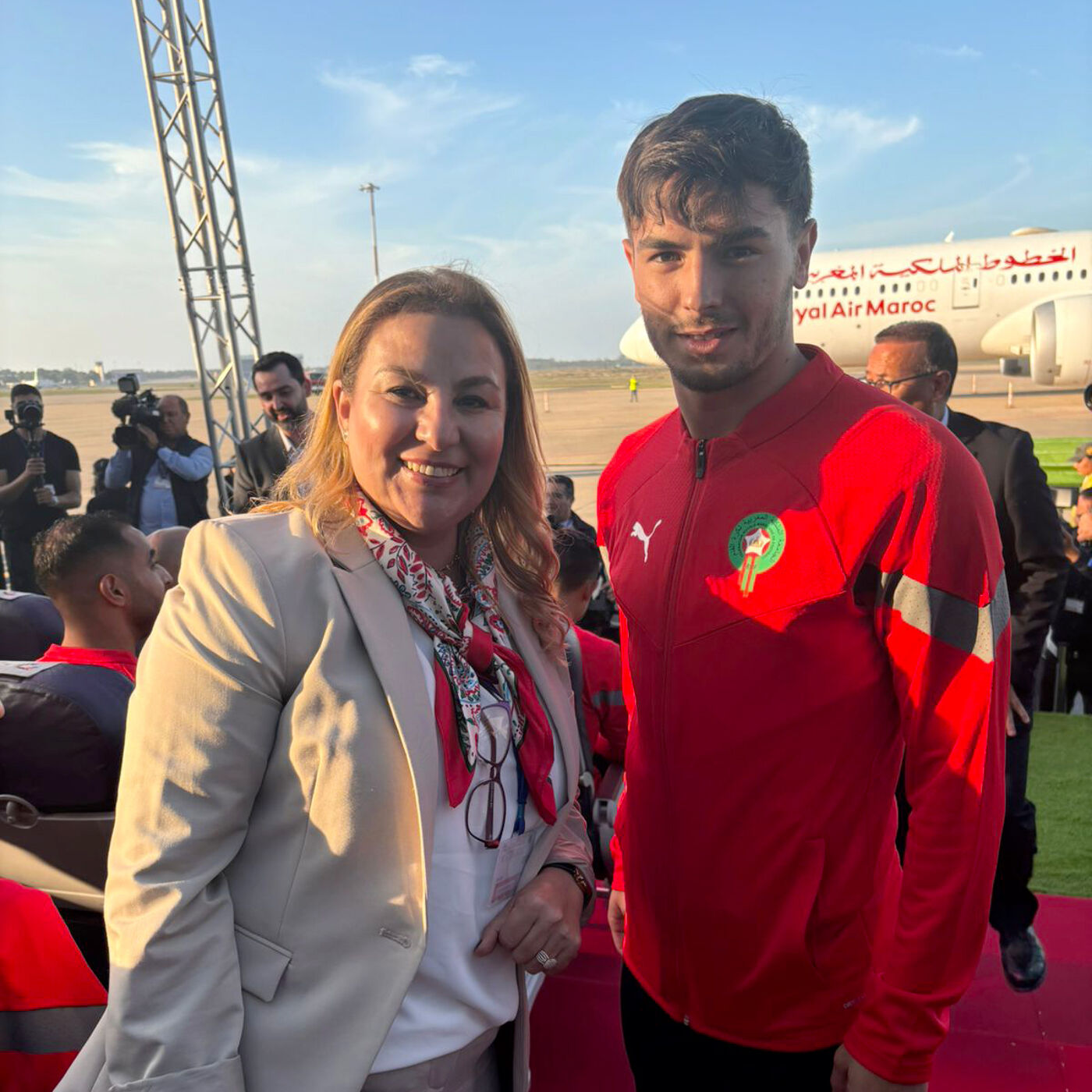 In the image, a man and a woman are standing together, smiling and posing for a picture. They are both wearing red shirts and appear to be at an airport.