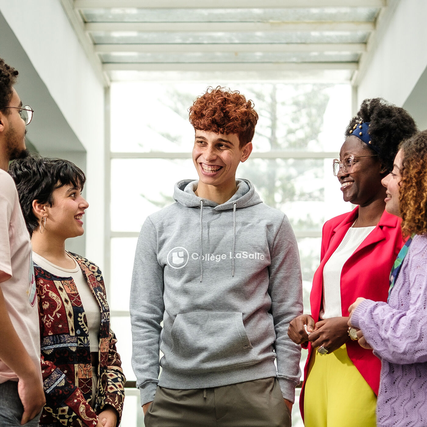 Five young adults in casual attire share a joyful conversation in a brightly lit indoor space, reflecting a lively and inclusive academic environment.