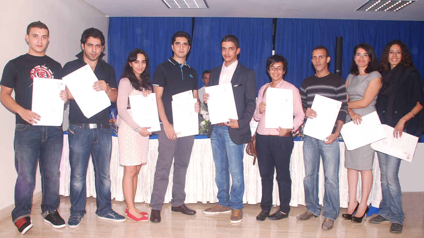 Nine jubilant individuals pose with graduation certificates, standing before a blue backdrop.