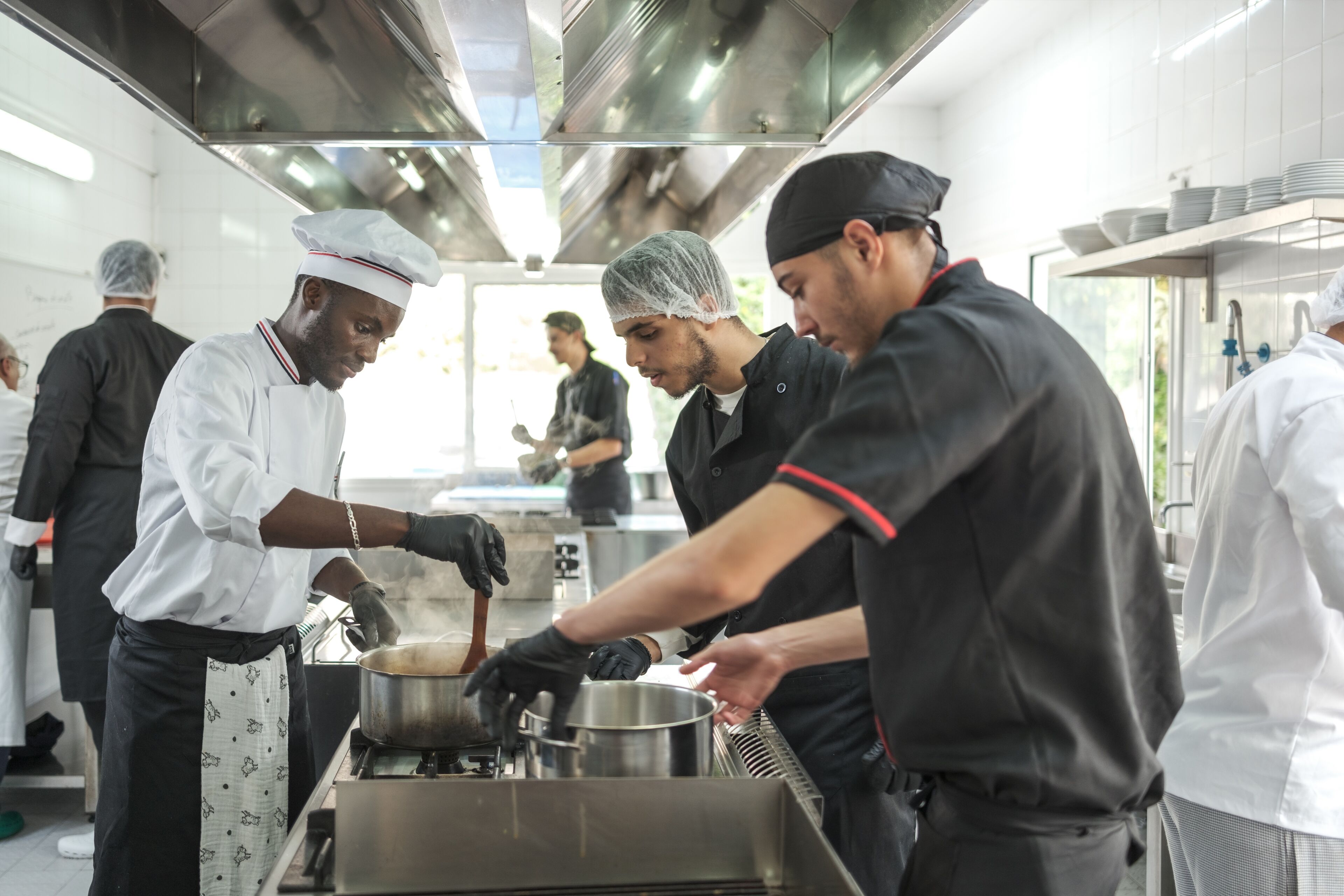Une équipe de chefs diversifiée cuisine et prépare des plats dans une cuisine de restaurant animée.