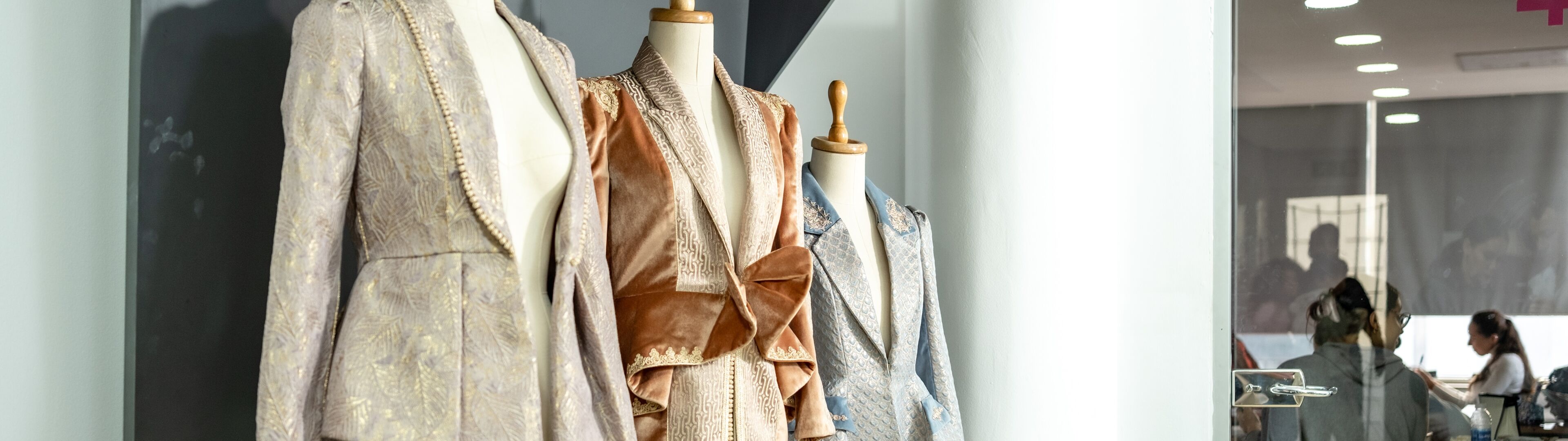 Des vestes de créateur sur mesure présentées sur des mannequins dans un atelier de création de mode, avec un travail en cours à l'arrière-plan.