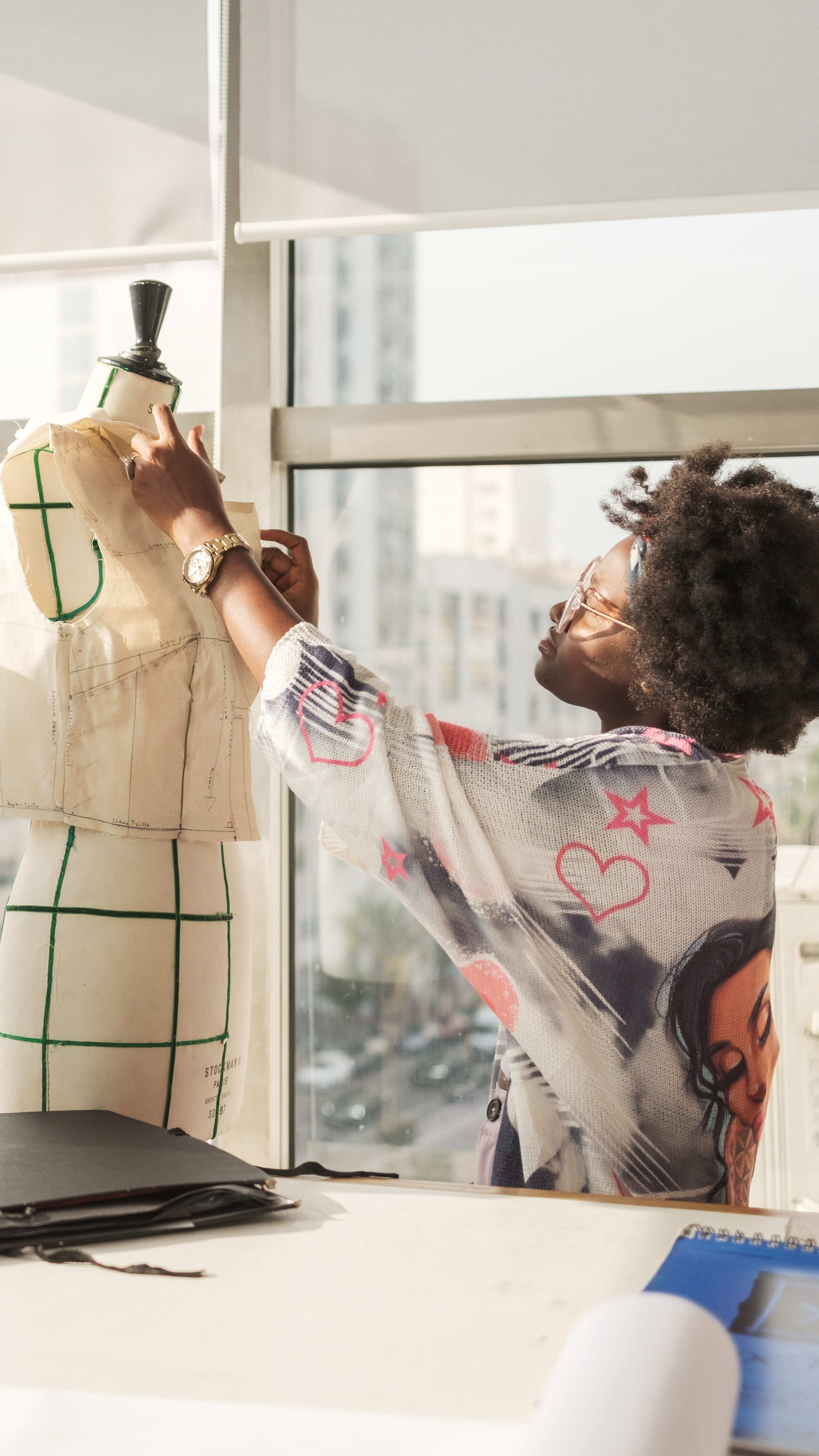 Une créatrice de mode perfectionne l'ajustement d'une robe sur un mannequin dans un atelier ensoleillé.