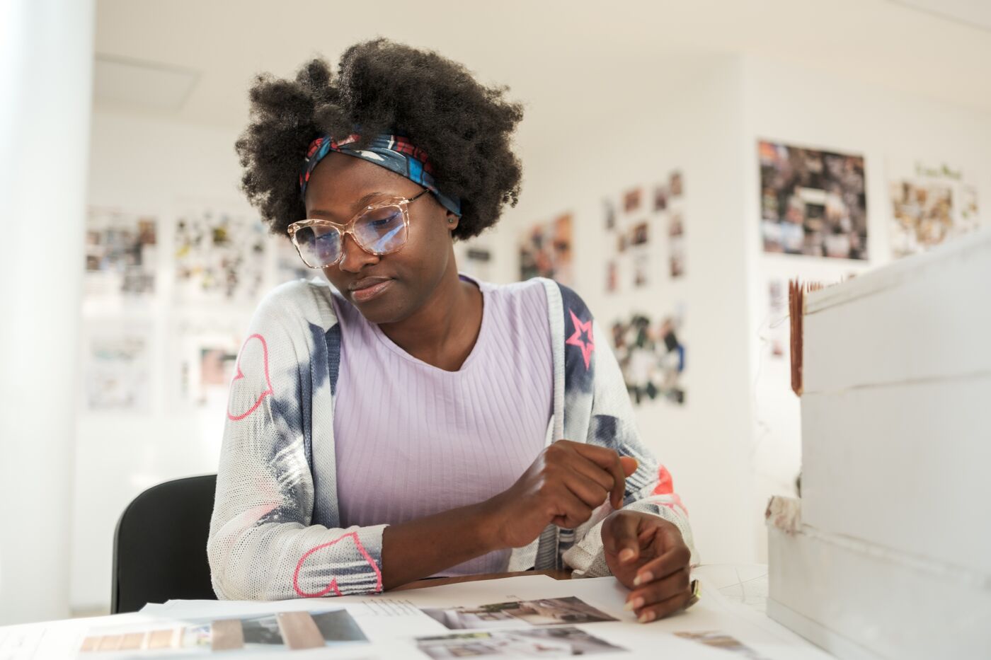 An artist with stylish glasses meticulously works on a project amidst a collage of inspiration on the wall.