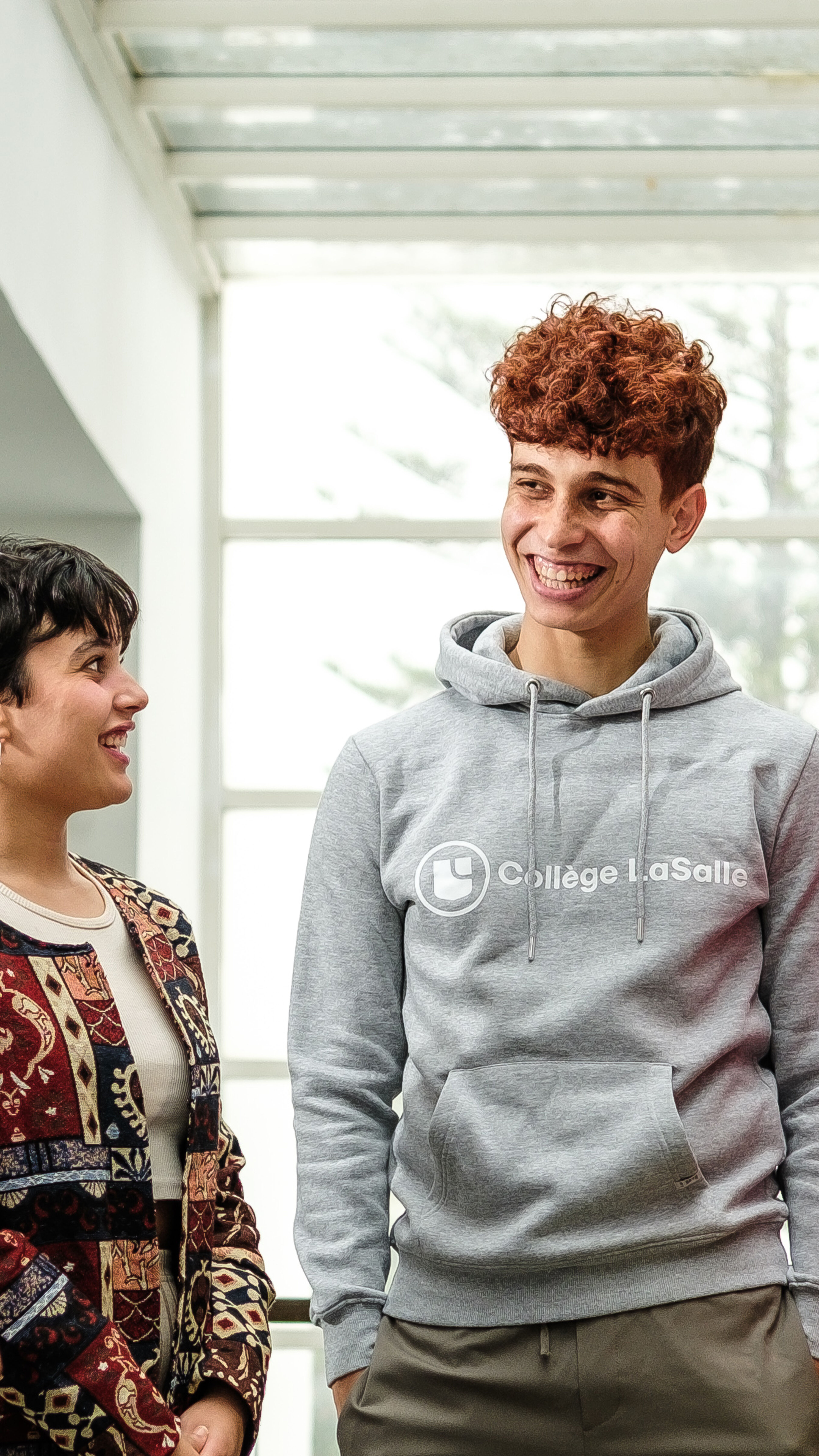 Five young adults in casual attire share a joyful conversation in a brightly lit indoor space, reflecting a lively and inclusive academic environment.

