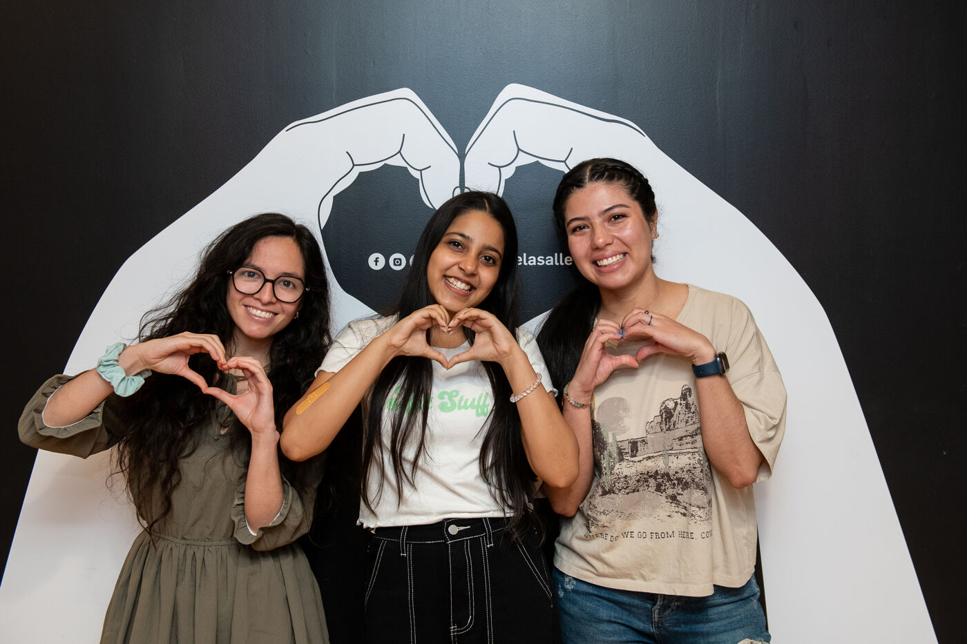 Three friends making heart shapes with their hands, sharing a moment of joy.