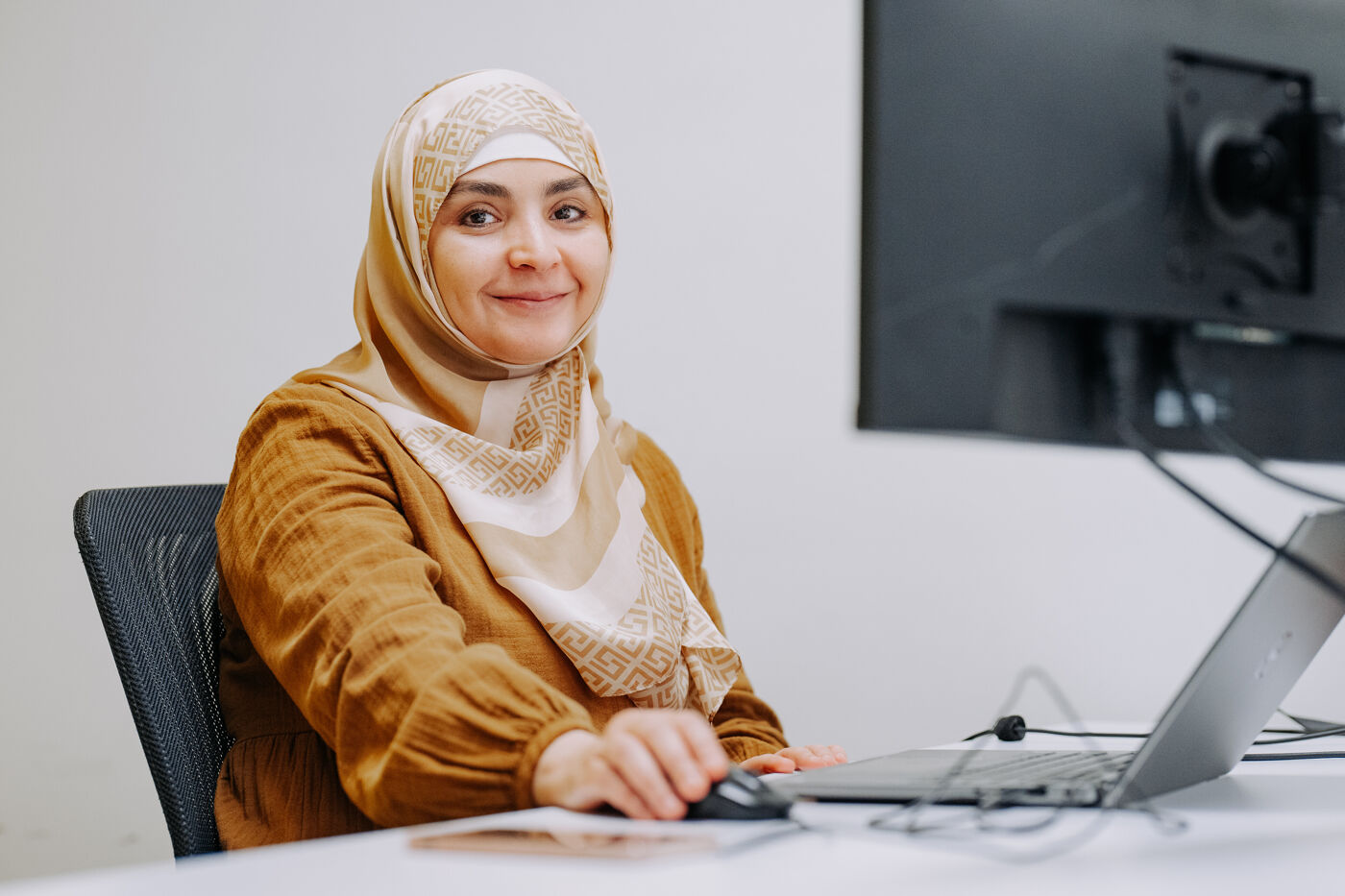 The image features a woman sitting at a desk, smiling, and using a laptop computer.