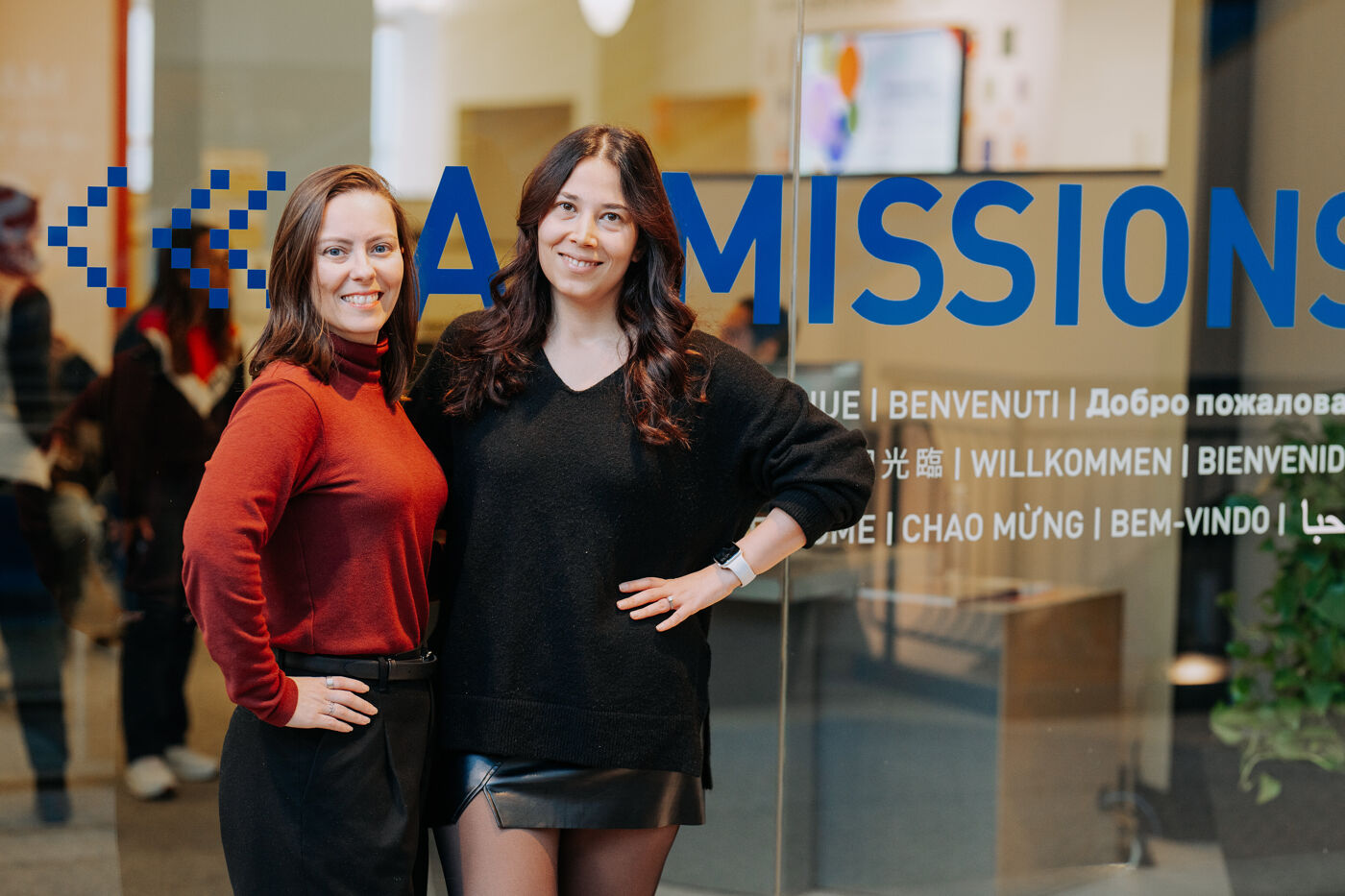 In the picture, there are two women standing in front of a glass door, posing for a photo.