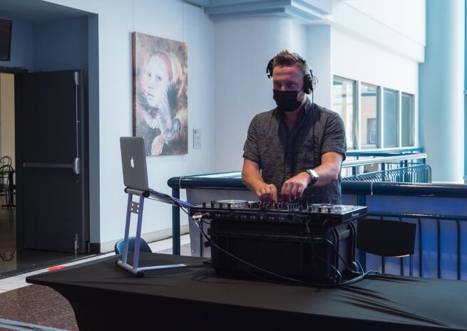 A focused DJ mixing music at a venue with a classic portrait in the background.