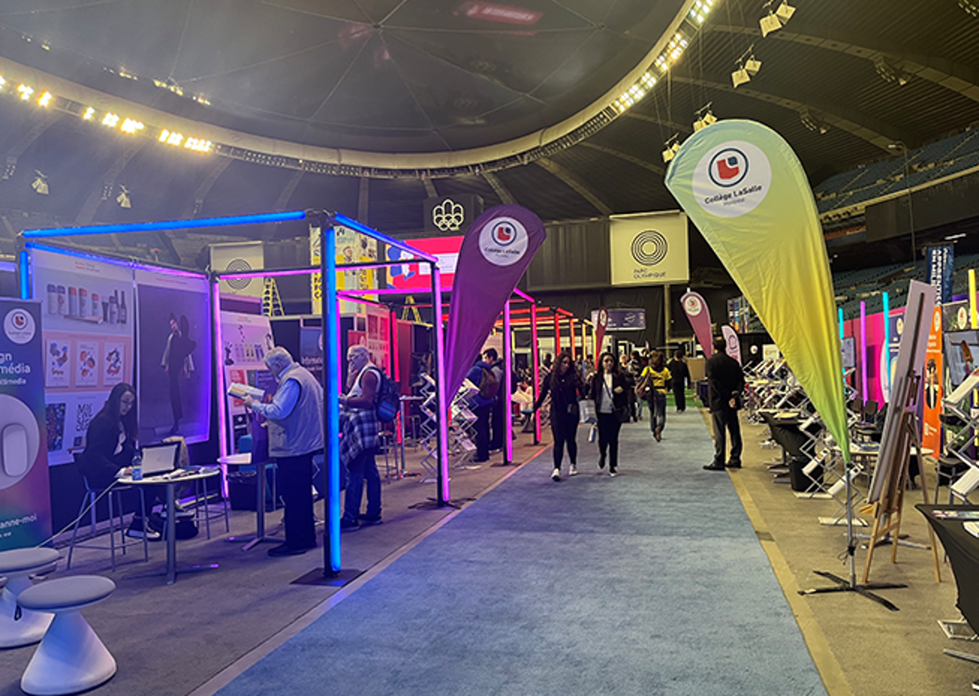 Attendees exploring various educational booths with vibrant displays and banners, including one for Collège LaSalle, inside an exhibition hall.