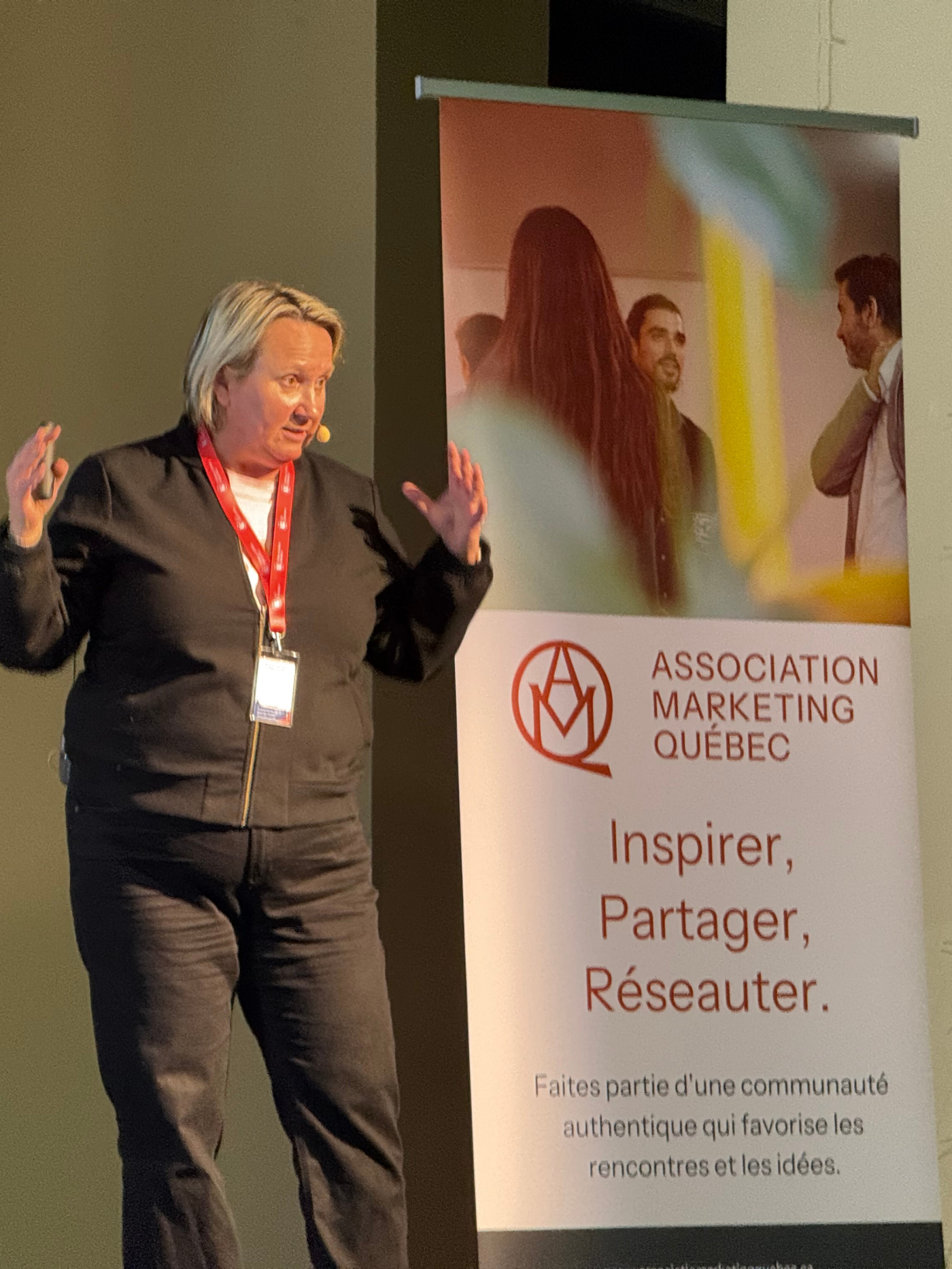 A woman speaks in front of a banner for the Association Marketing Québec, which reads "Inspire, Share, Network".