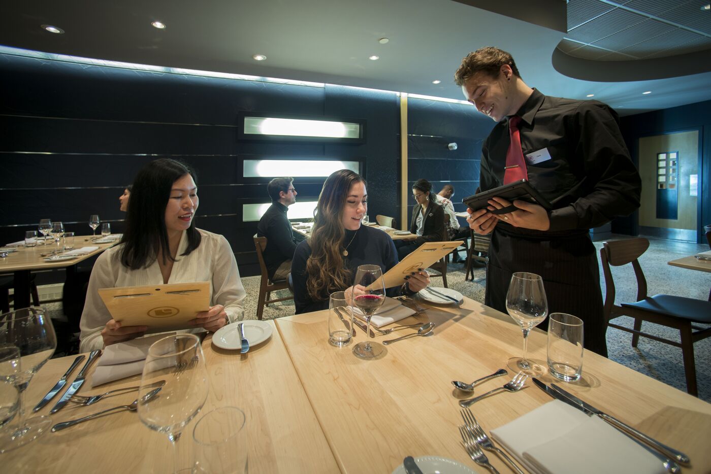 Guests exploring the menu with the assistance of a cheerful waiter at an elegant restaurant.