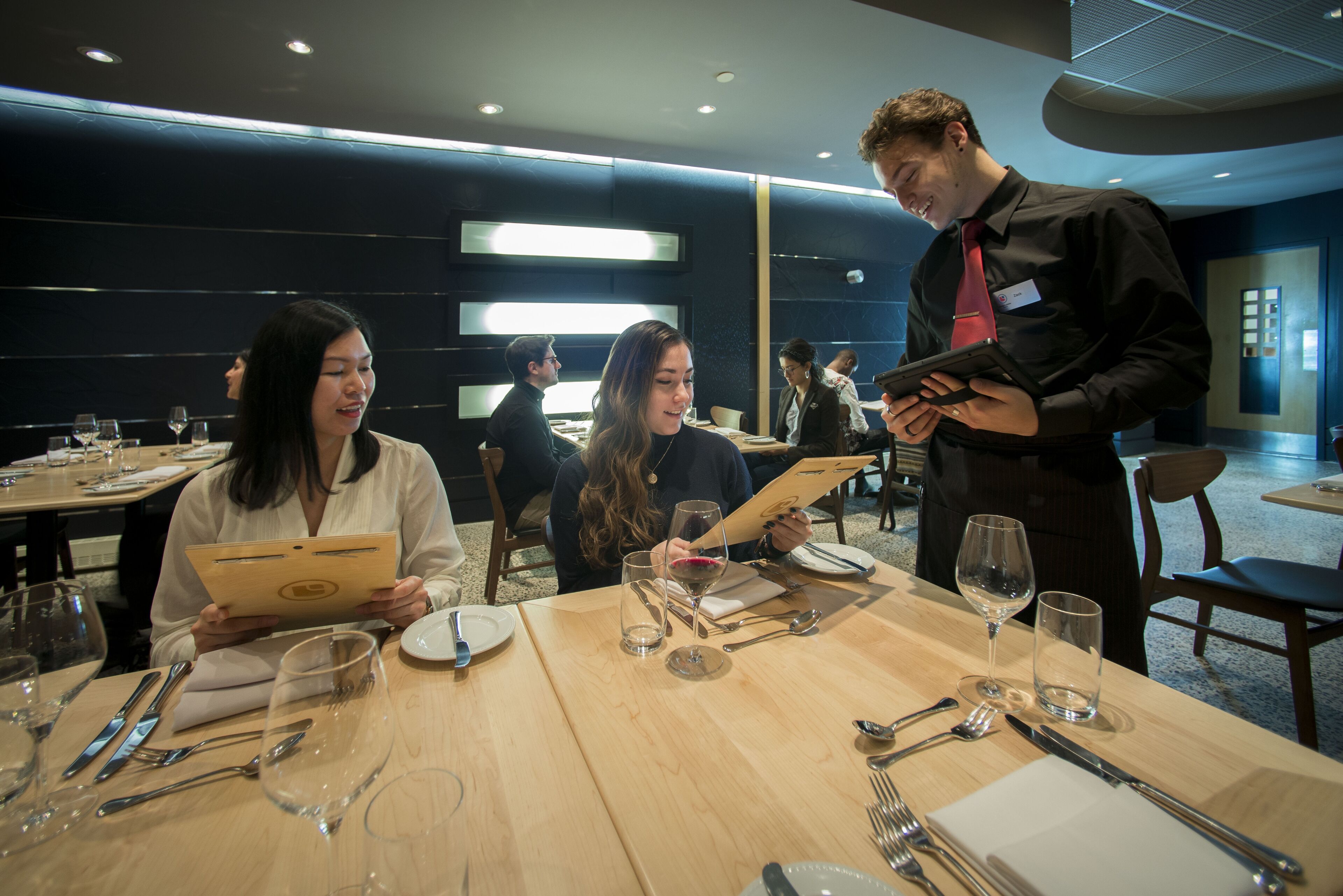 Guests exploring the menu with the assistance of a cheerful waiter at an elegant restaurant.