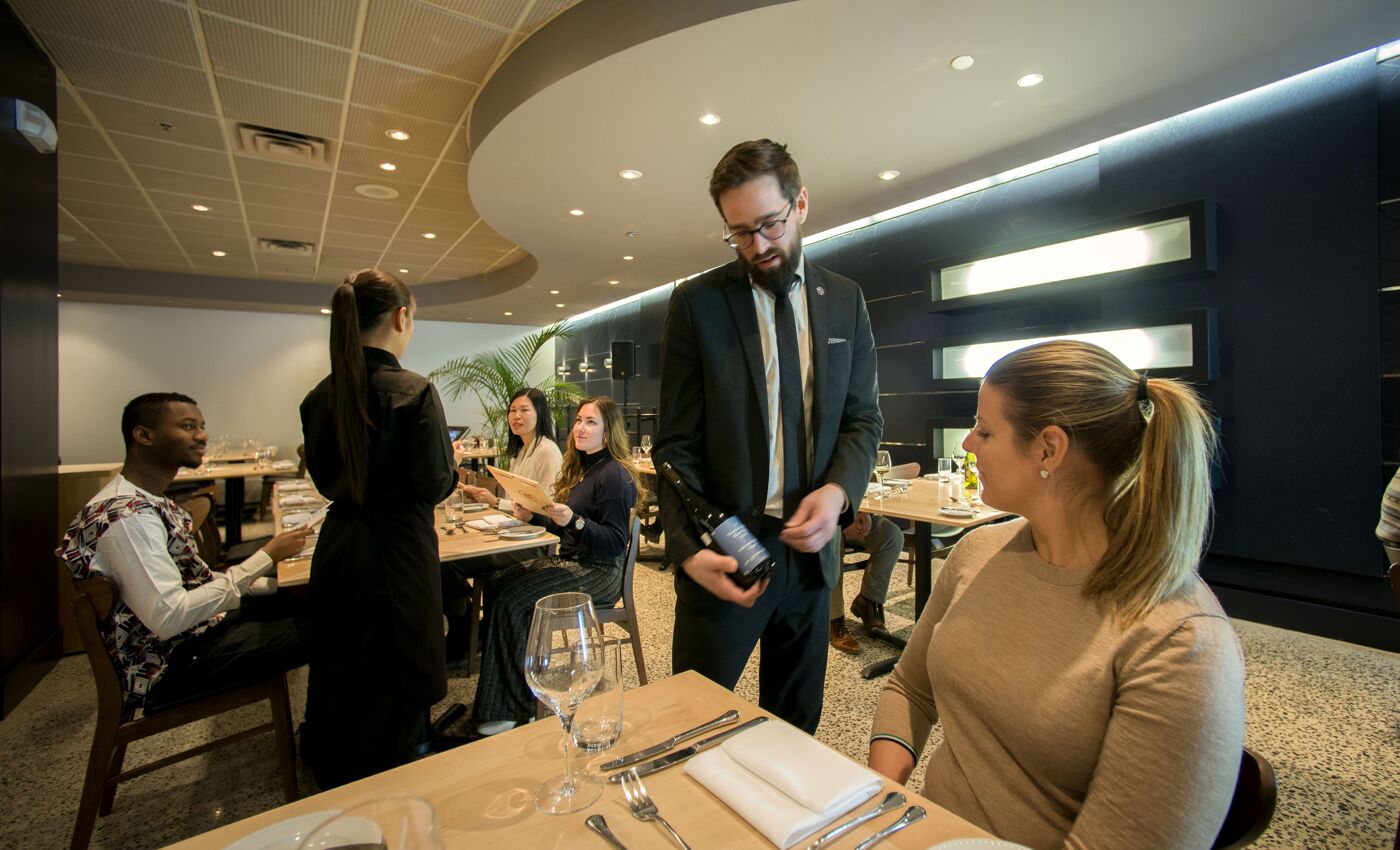 A sommelier presents a selection of wine to diners at a modern, sophisticated restaurant setting.