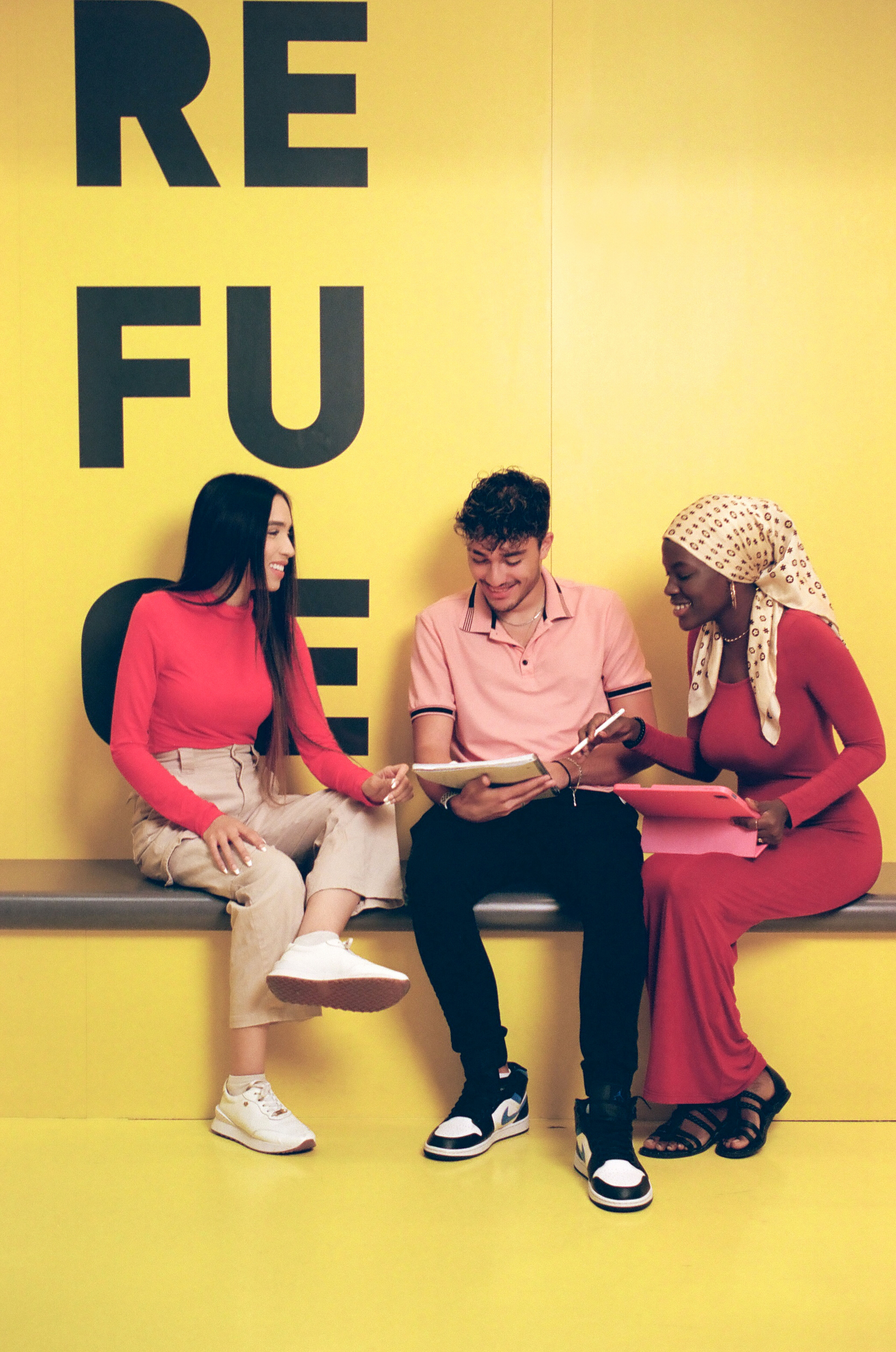 Three students engage in a lively discussion, with a vibrant yellow backdrop highlighting their camaraderie.