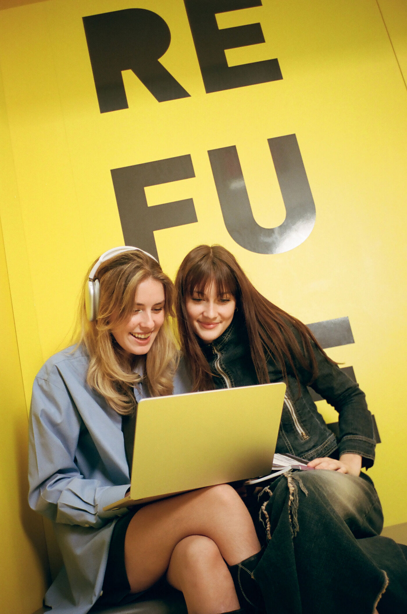 Two friends share headphones and a screen, enjoying a moment of mutual interest.