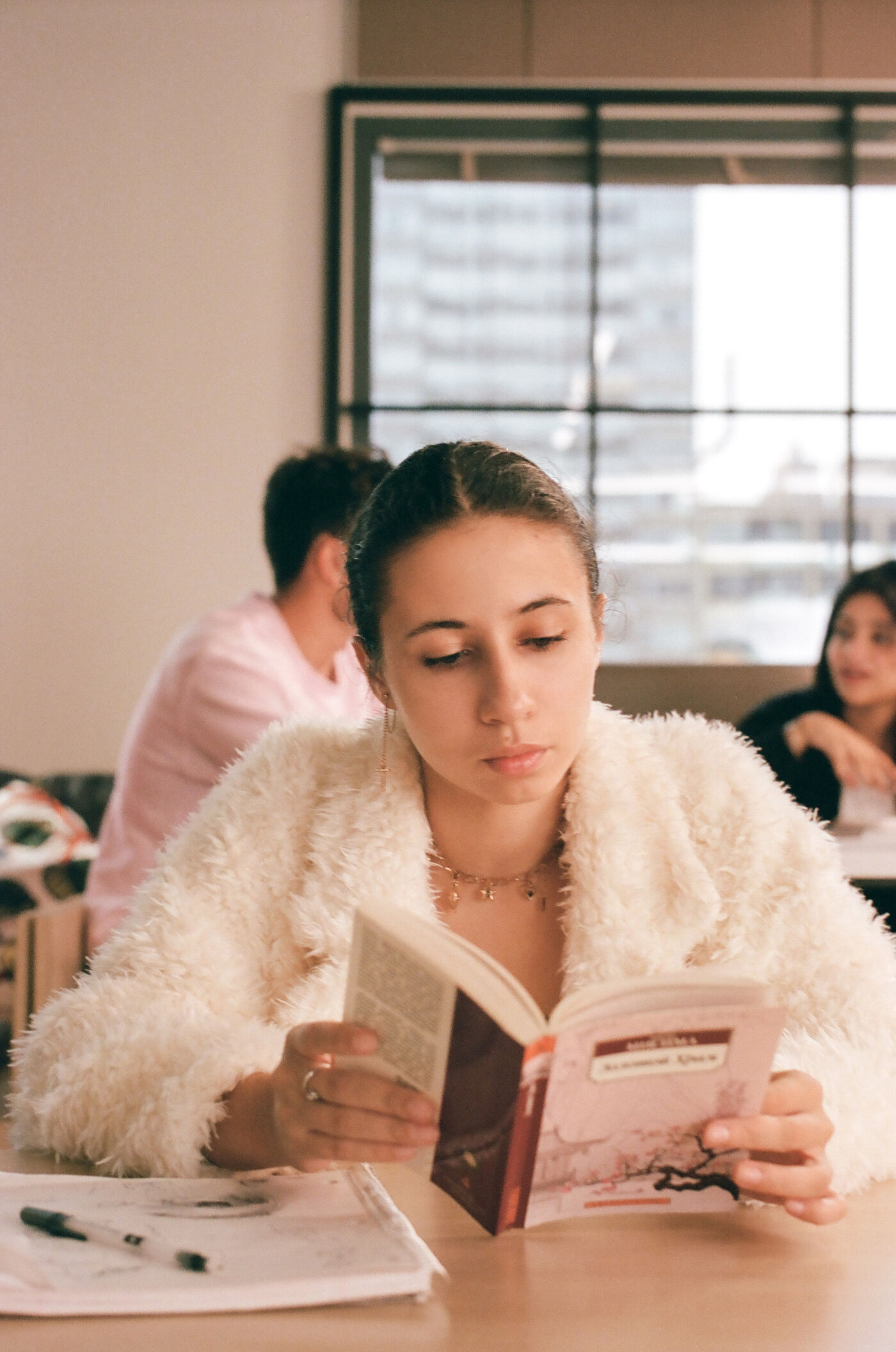 A student delves into her book amidst a classroom setting, her concentration palpable.