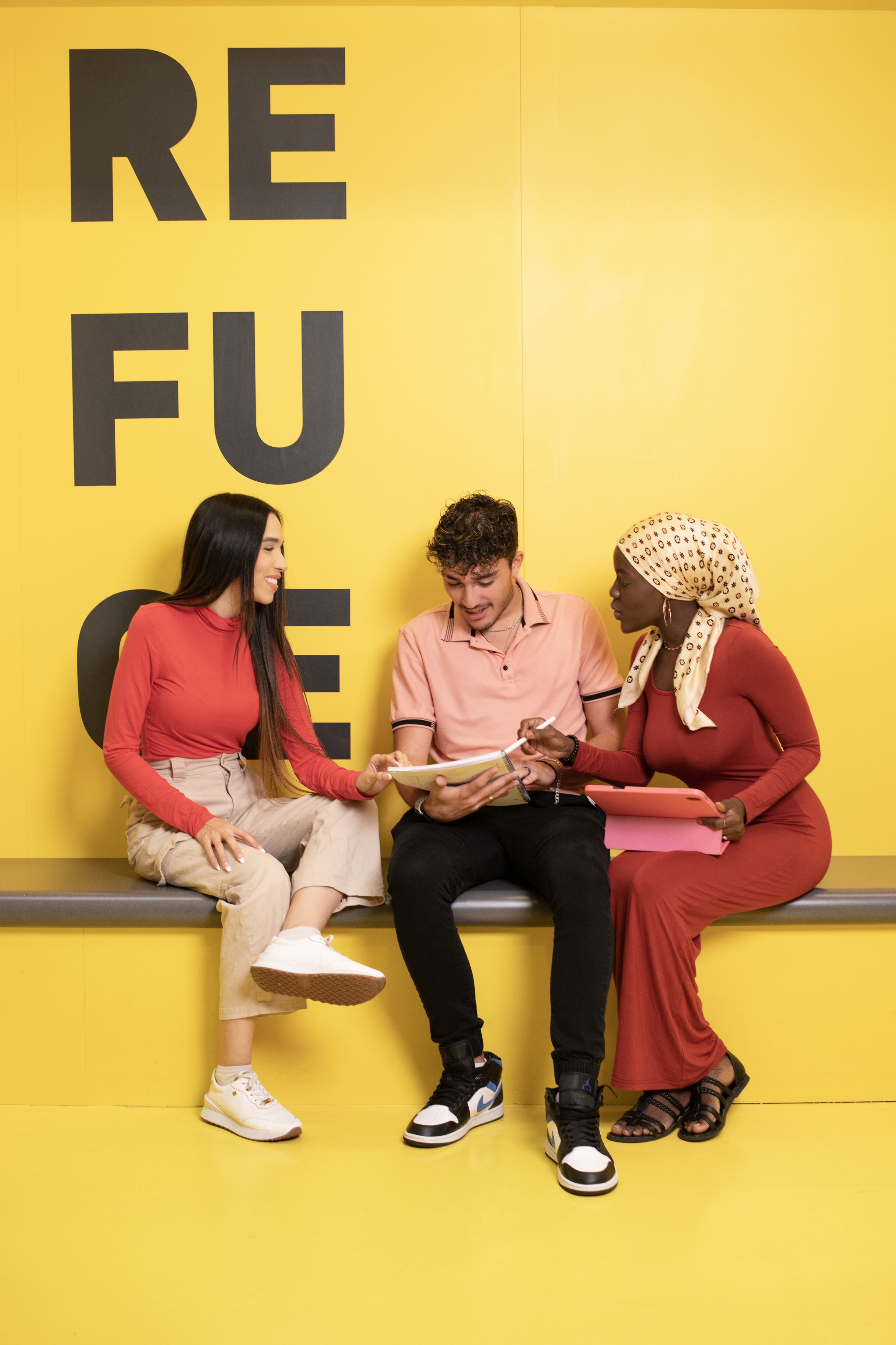 Three peers share ideas in an animated discussion, framed by a bold yellow wall that evokes energy and creativity.