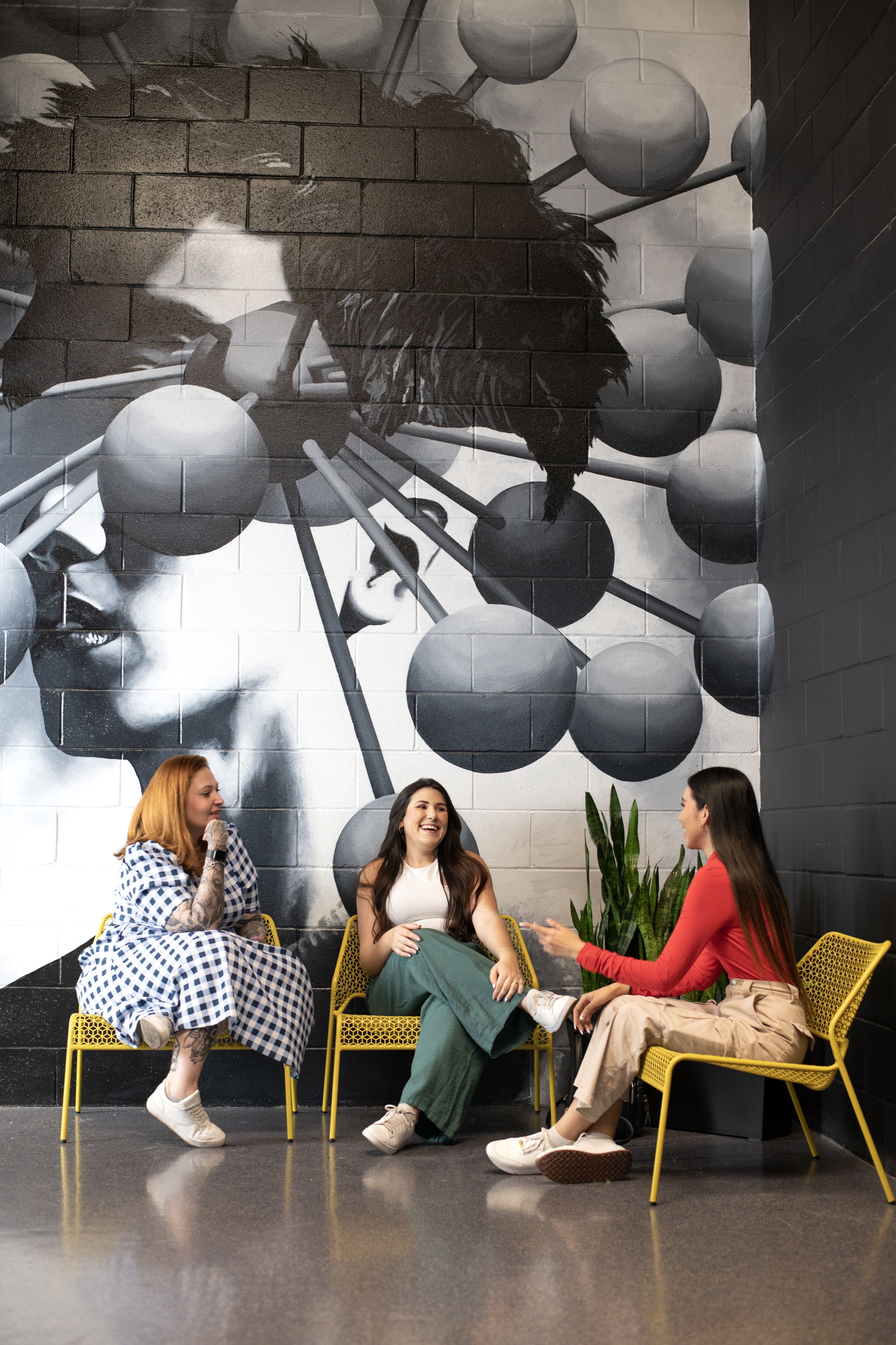 Three friends enjoy a lively discussion in a creatively inspired space with striking wall art.