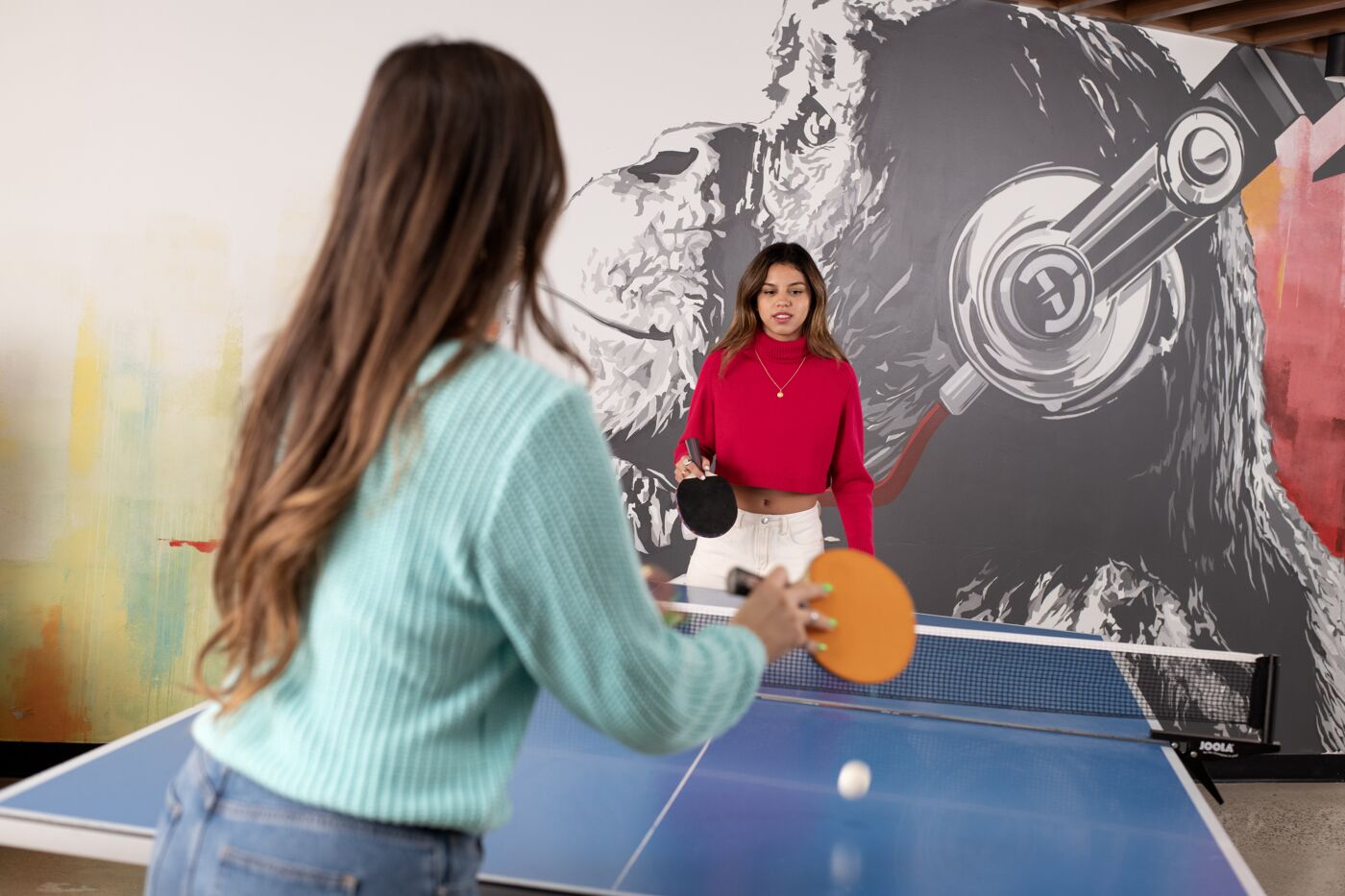 Students enjoying a friendly game of table tennis with artistic graffiti in the background.