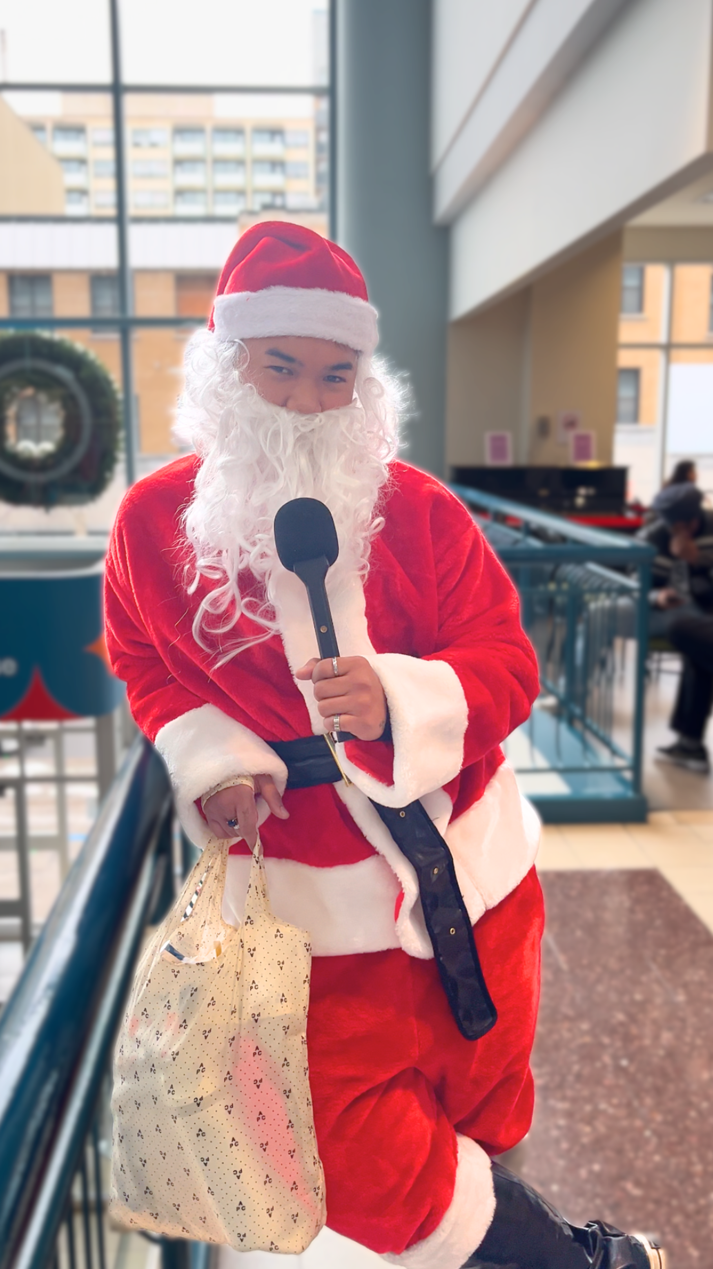 The image features a man dressed as Santa Claus holding a microphone and standing in a room.