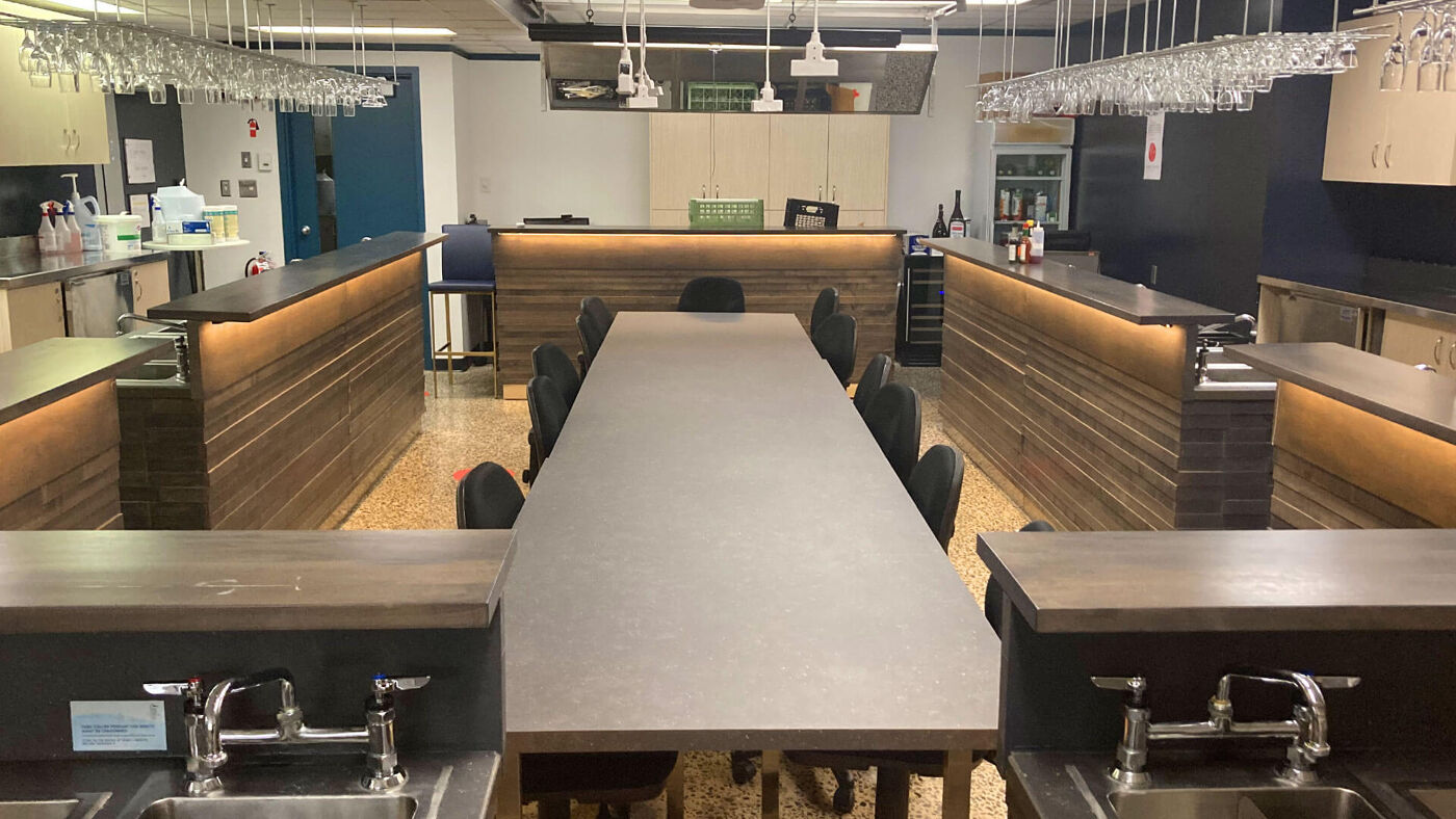 A sleek, contemporary office kitchen with a long dining table, bar seating, and hanging glassware storage, showcasing a professional and welcoming space.