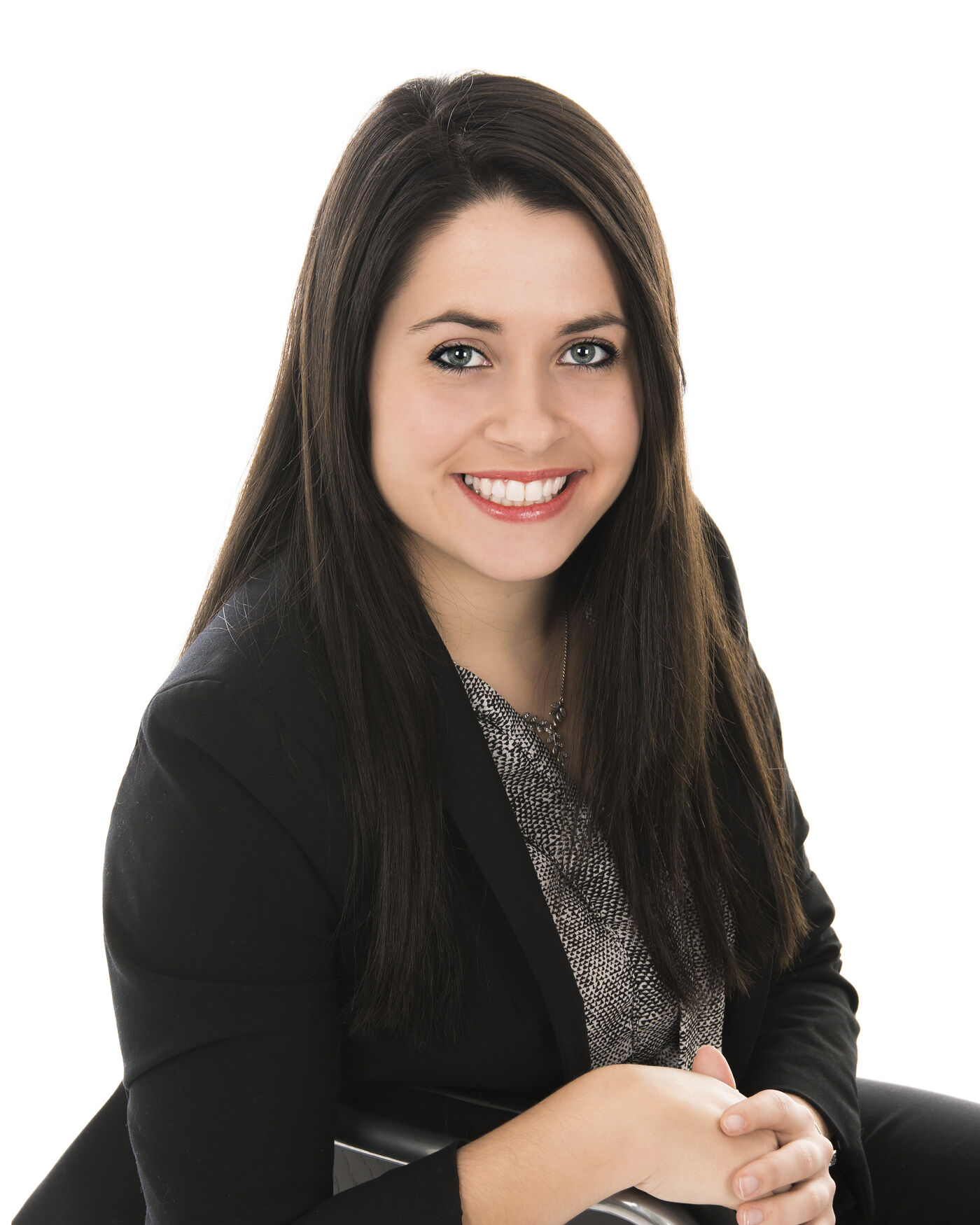 A well-groomed woman with long dark hair smiling at the camera, wearing a black blazer over a patterned blouse, white background.