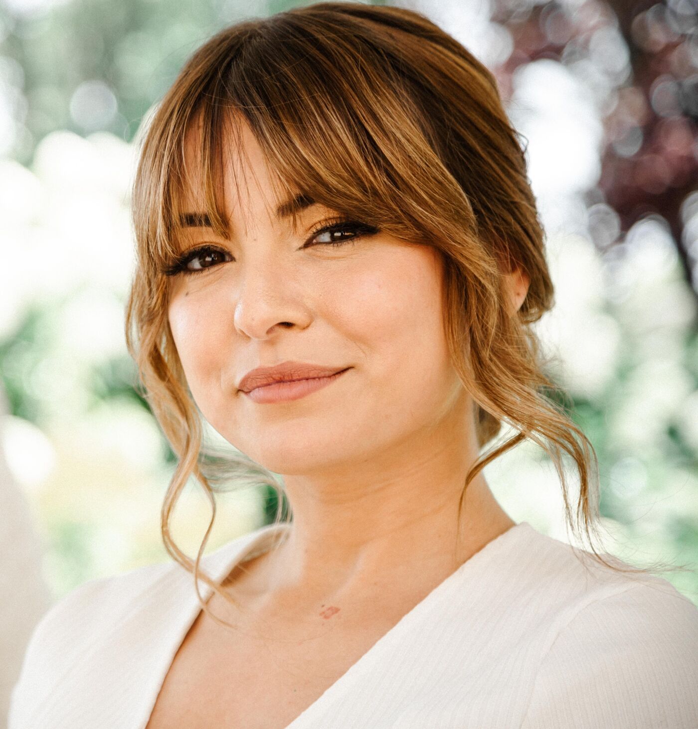 A woman with a warm smile and a stylish updo in a chic white outfit, exuding confidence.