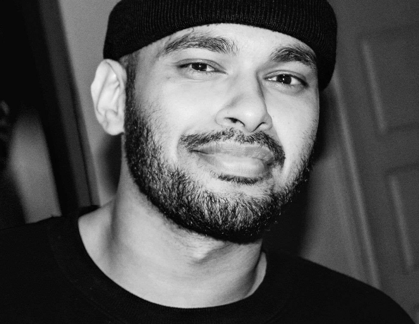 A content man sporting a beanie and a casual t-shirt, with a slight smile, in a black and white photo.