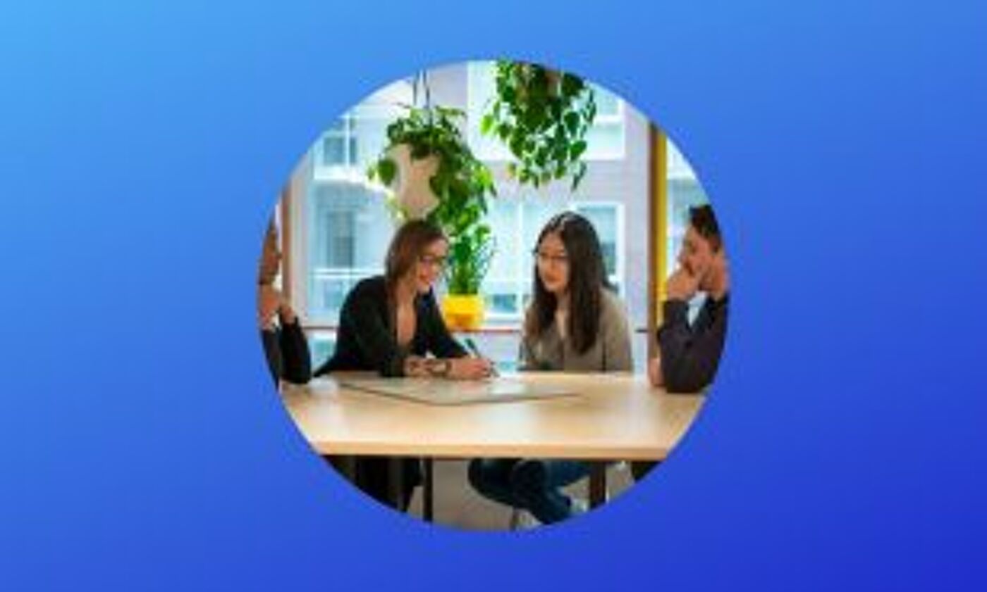 Four individuals actively participating in a meeting at a table in a modern office setting.