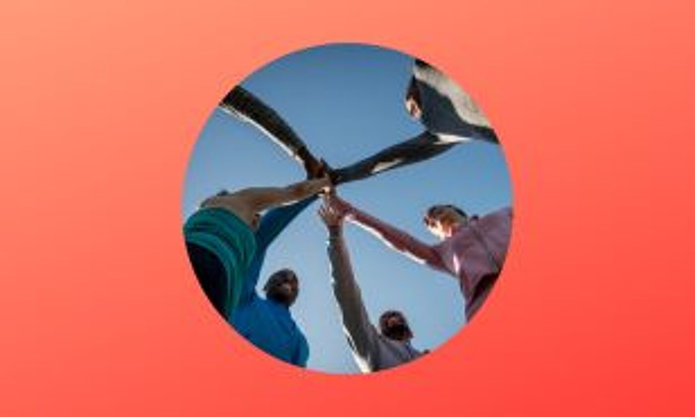 A group of individuals participate in a team-building activity, touching hands in a circular formation against a clear sky, symbolizing cooperation and unity.