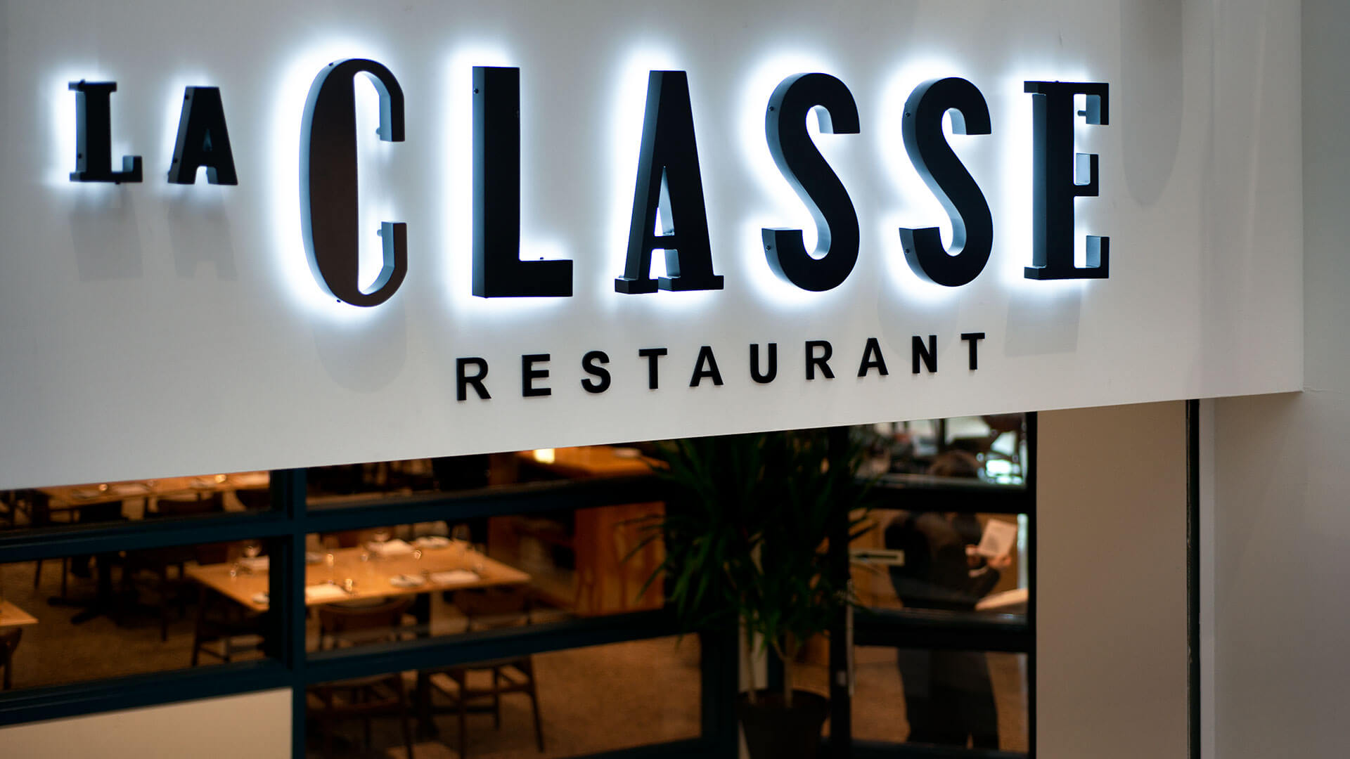 Illuminated signage for "La Classe Restaurant" with a cozy dining area visible in the background.