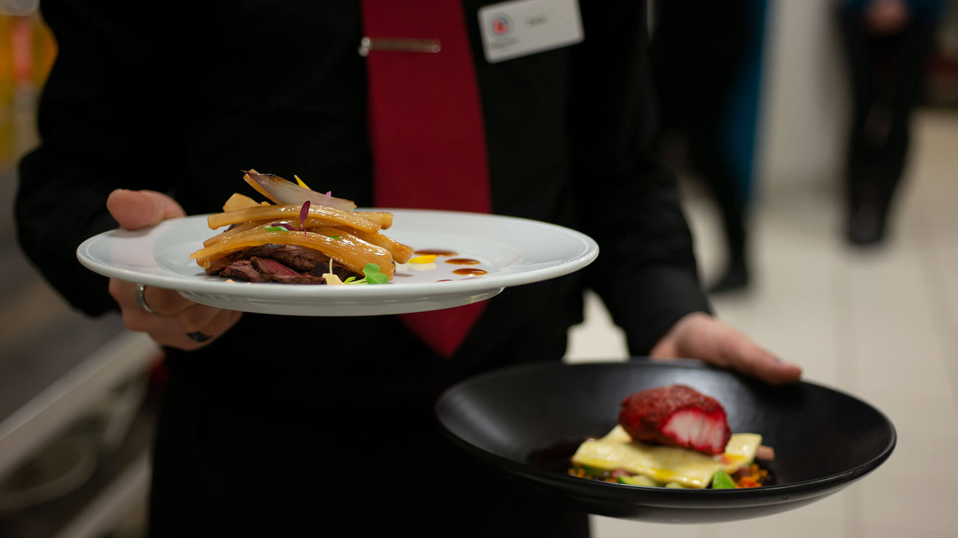 Un serveur présentant deux plats sophistiqués, mettant en valeur des techniques de dressage de la haute gastronomie.