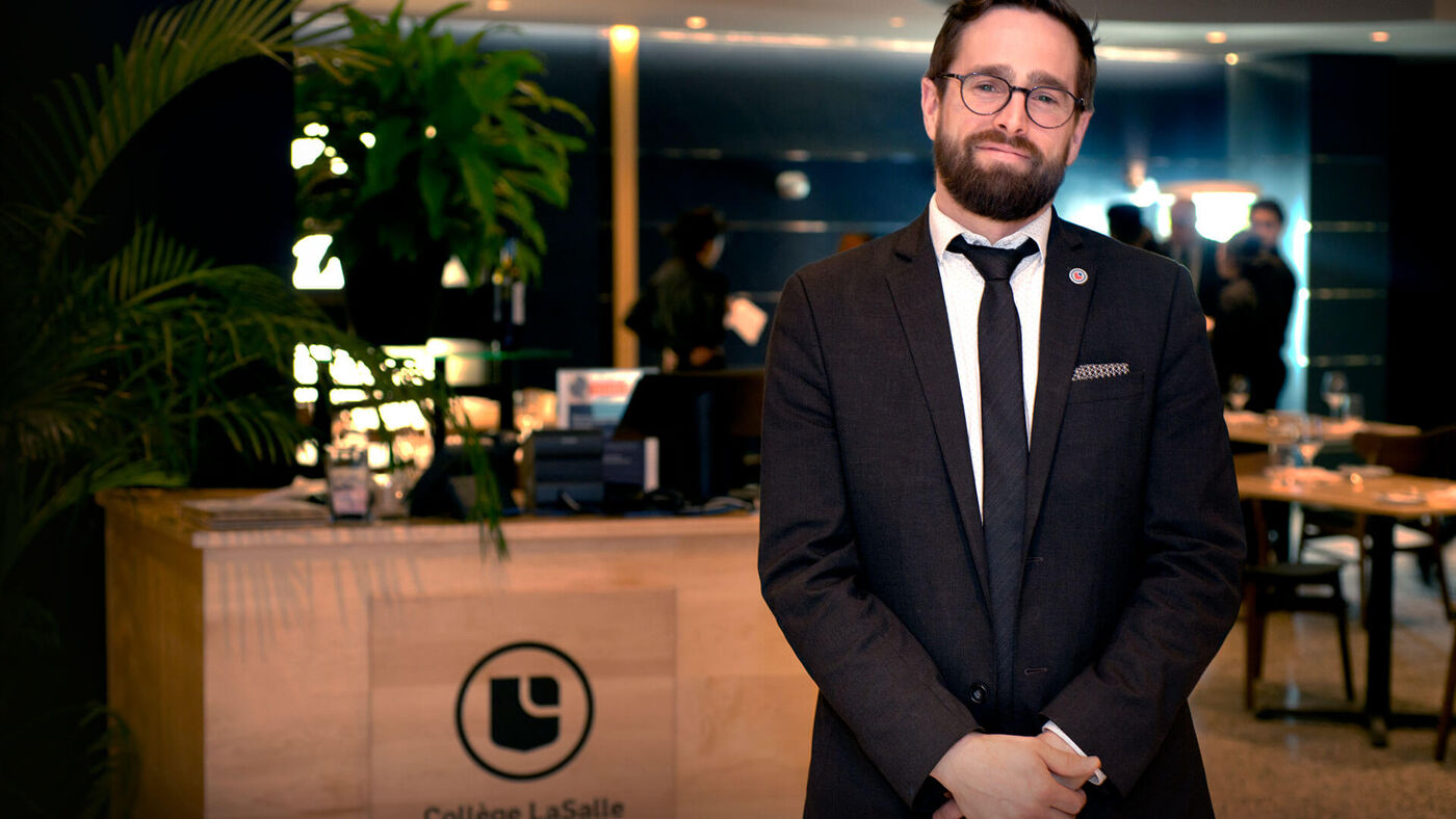 A professional host in a formal suit stands confidently in the elegant setting of a restaurant associated with College LaSalle.