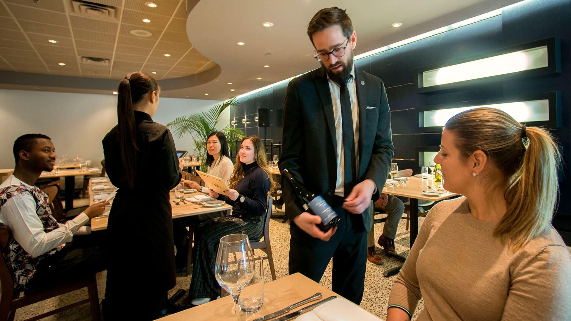 Un serveur s'occupe des invités dans un restaurant géré par un collège, enrichissant l'ambiance éducative avec une expérience de service pratique.