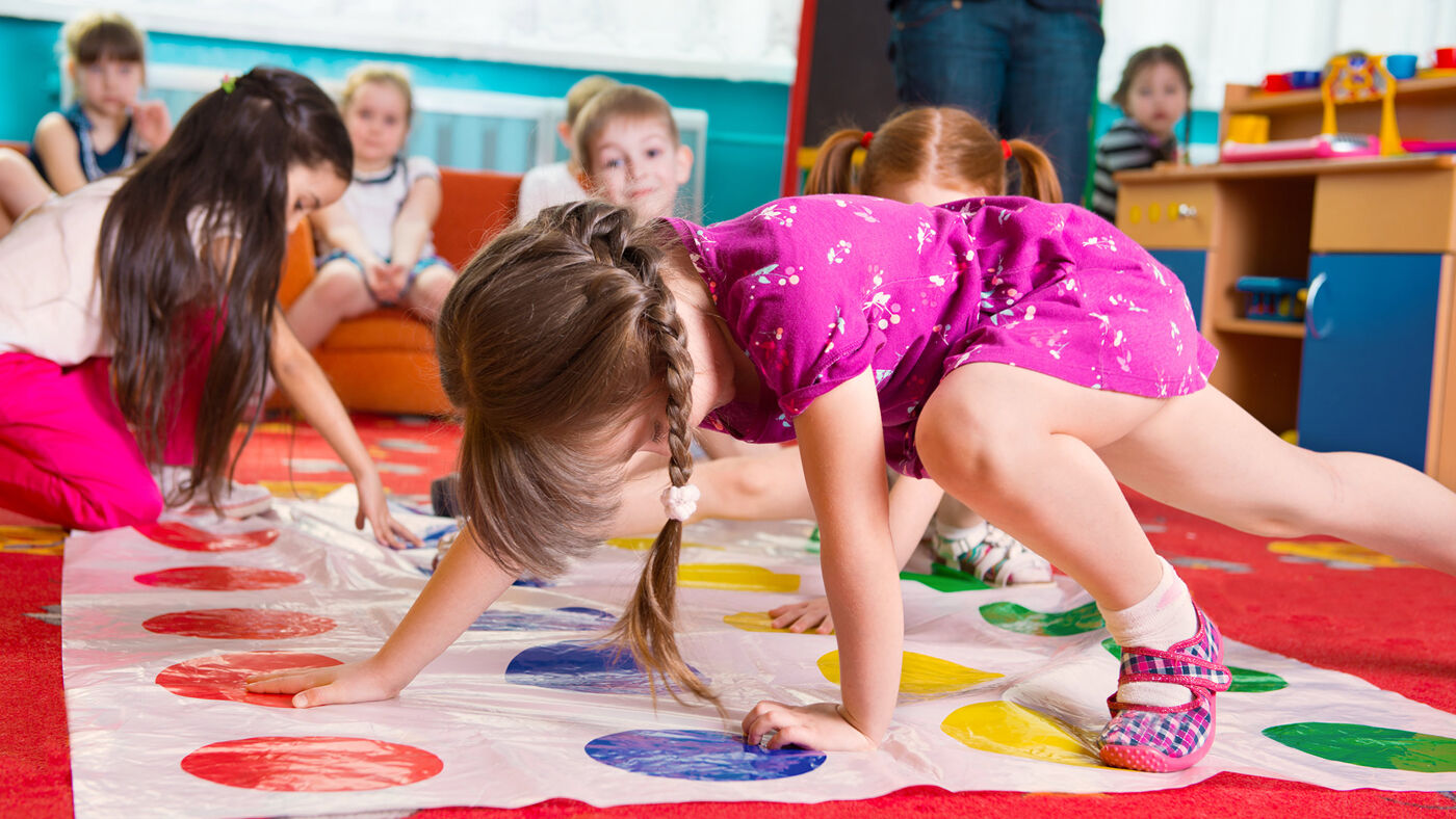 Children engaged in a game of Twister in a colorful classroom setting, showcasing movement and playfulness.