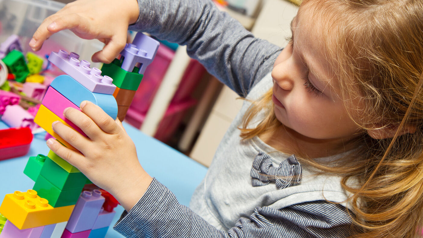 A young girl focused on assembling colorful building blocks, expressing creativity and concentration.