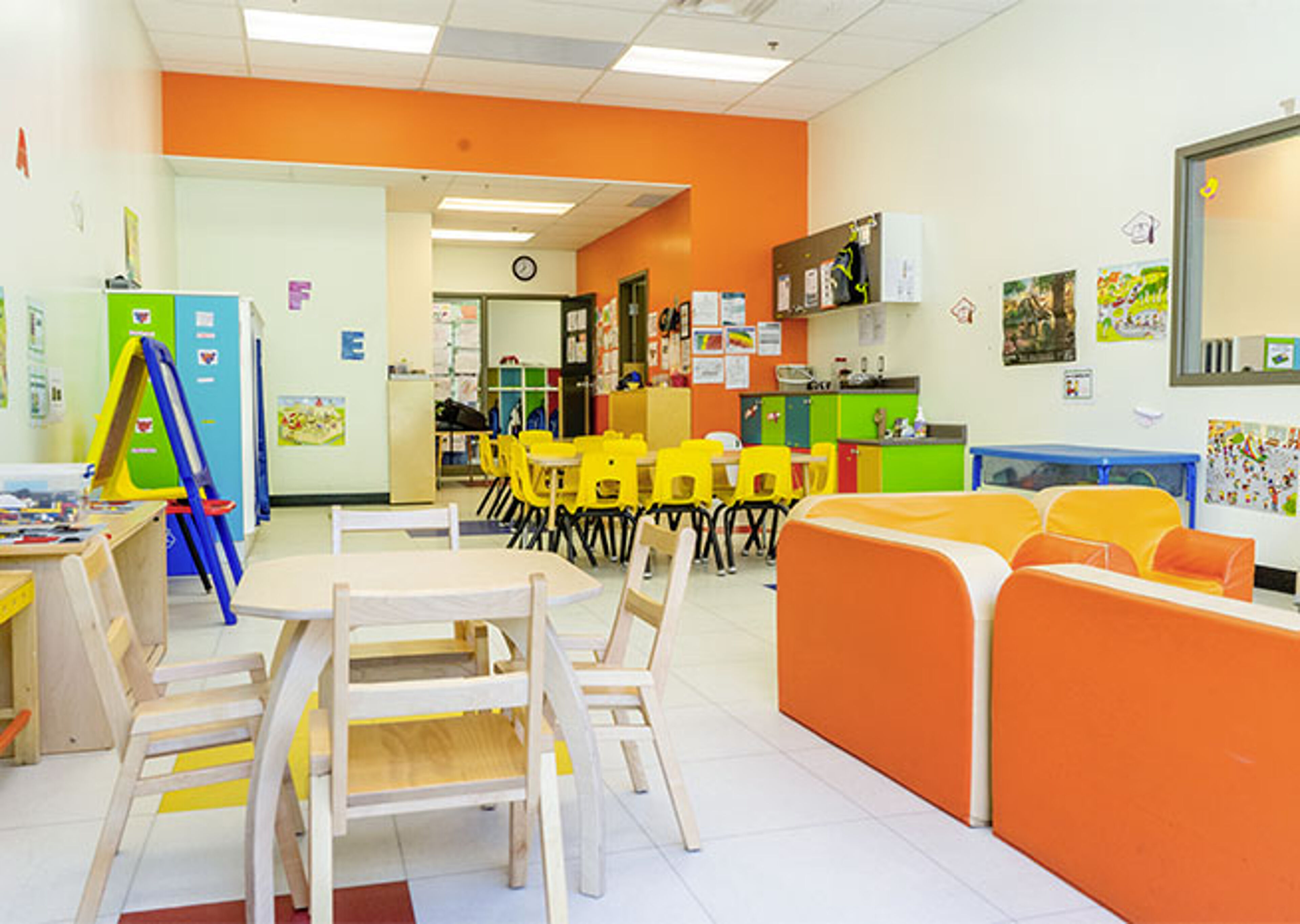  An orderly preschool classroom featuring a kitchen playset, a blue sofa, and blue chairs at tables, ready for learning activities.