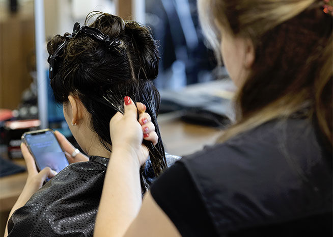 Un coiffeur travaillant sur un chignon d'une cliente qui utilise un smartphone, dans un salon de coiffure.