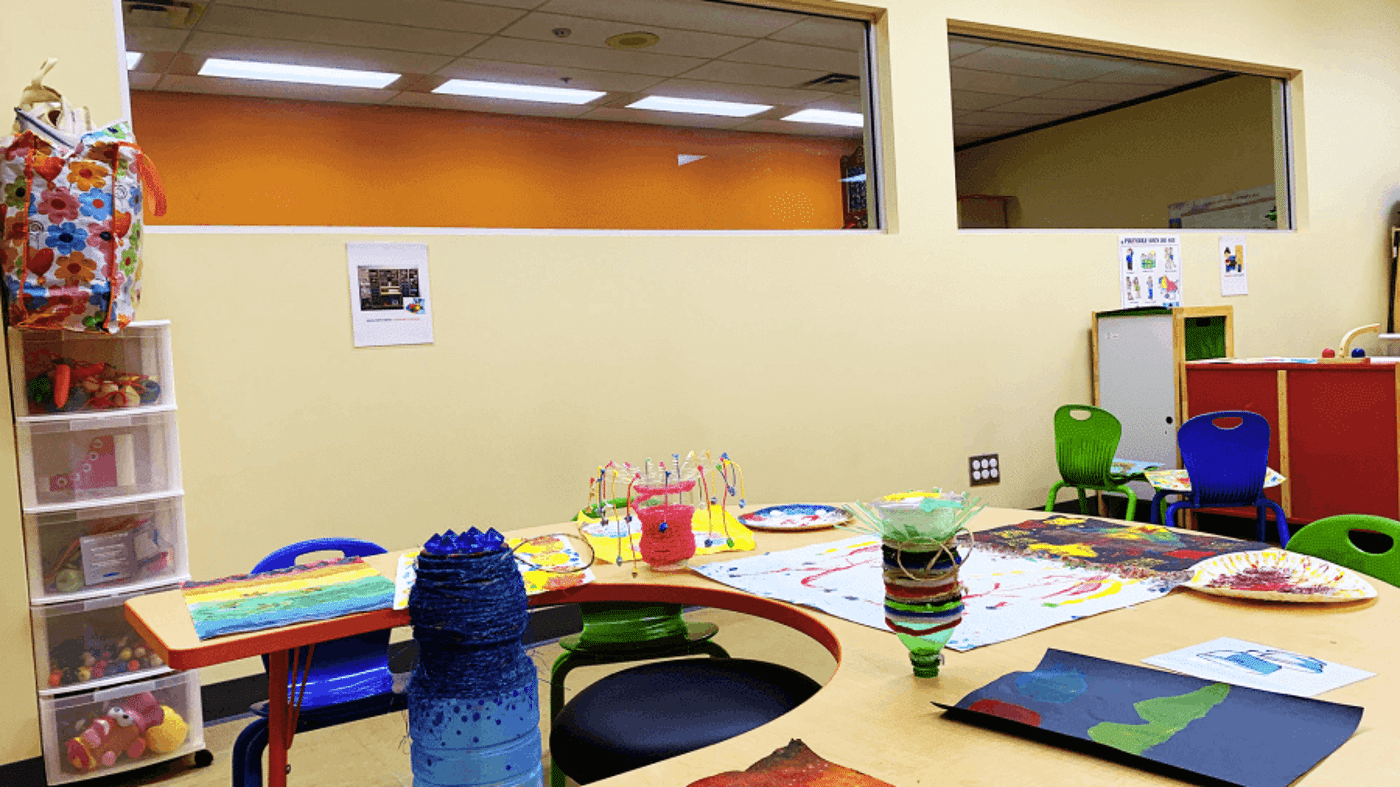 A colorful art classroom with a painting station for children, supplies on shelves, and artwork on display.