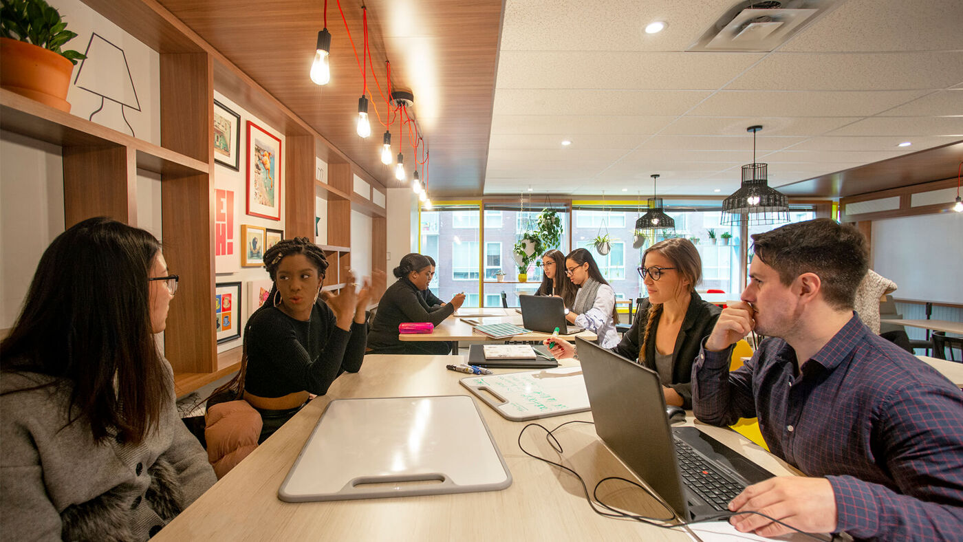 A group of professionals engaged in a discussion at a long table in a bright, modern co-working space.