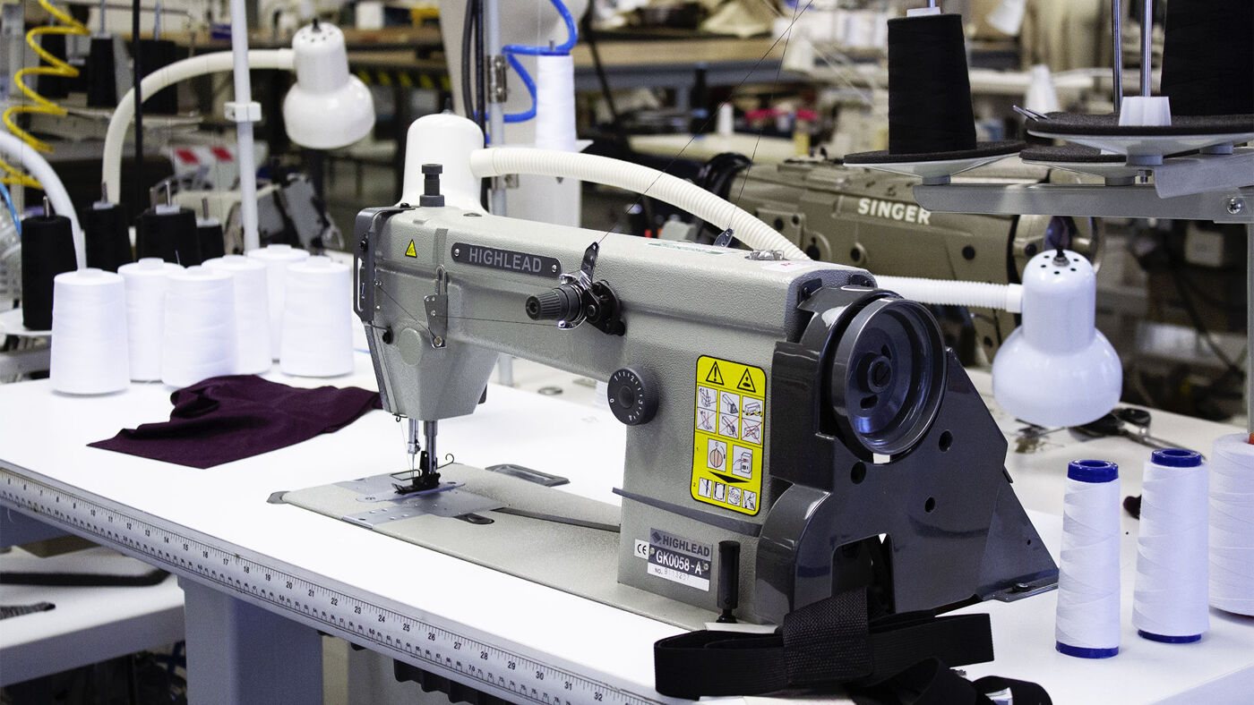 Close-up of an industrial sewing machine with spools of thread on the workbench in a textile manufacturing setting.