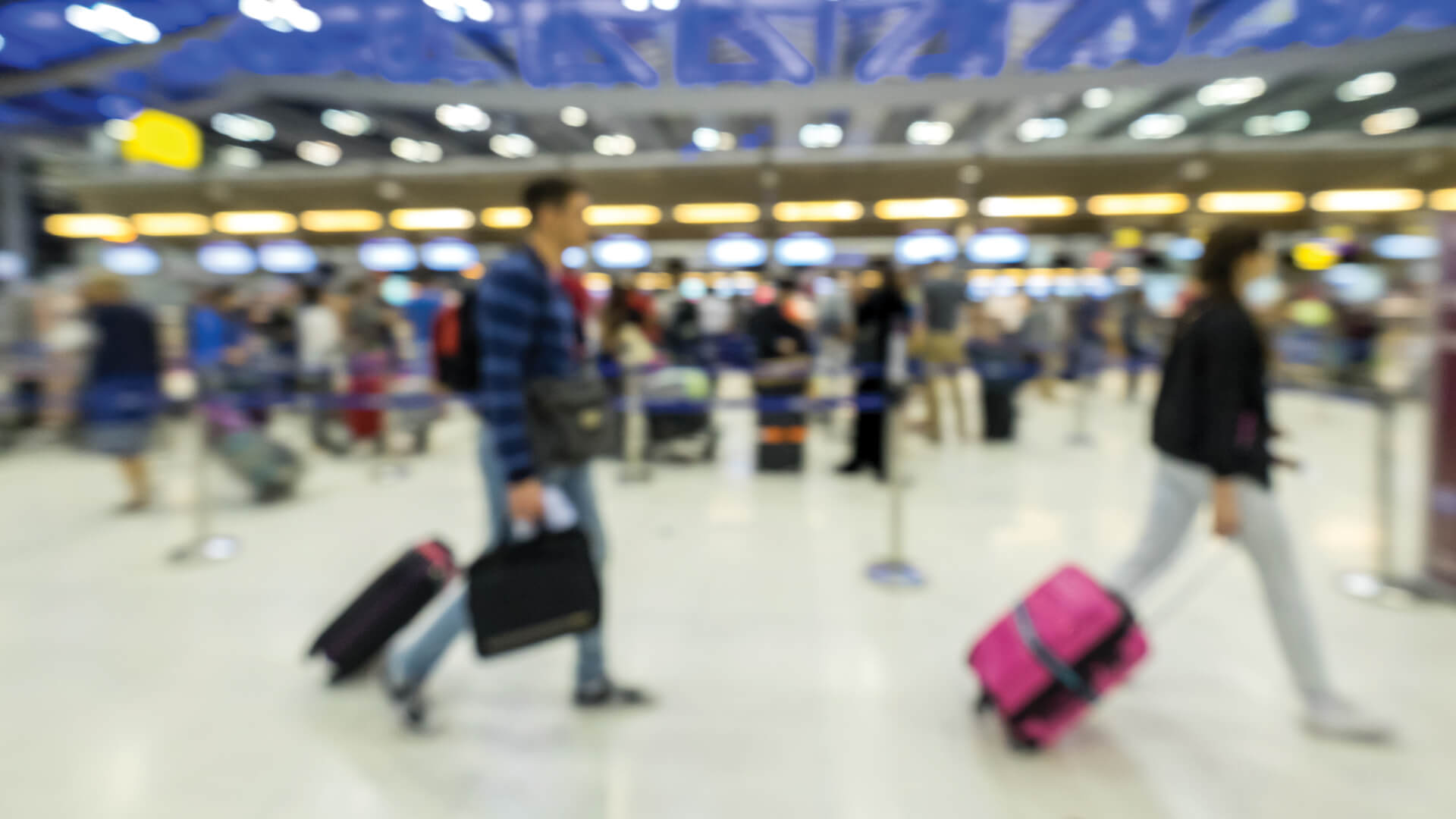 A defocused image of passengers with luggage in a busy airport terminal, capturing the hustle of travel.
