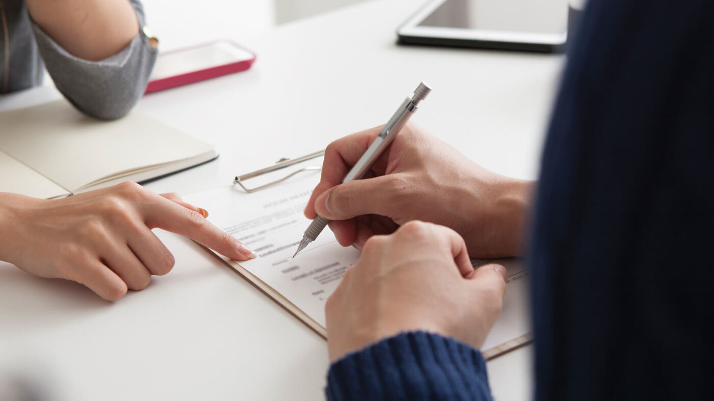Two individuals collaborating on a job application, with one holding a pen and pointing to a specific section of the document.