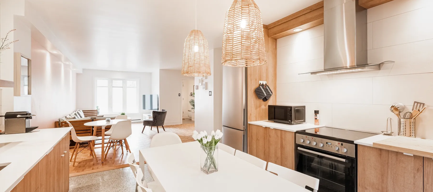 The image features a kitchen with a dining table, chairs, a refrigerator, and a microwave. There are also potted plants and flowers on the table, adding a touch of decoration to the space.