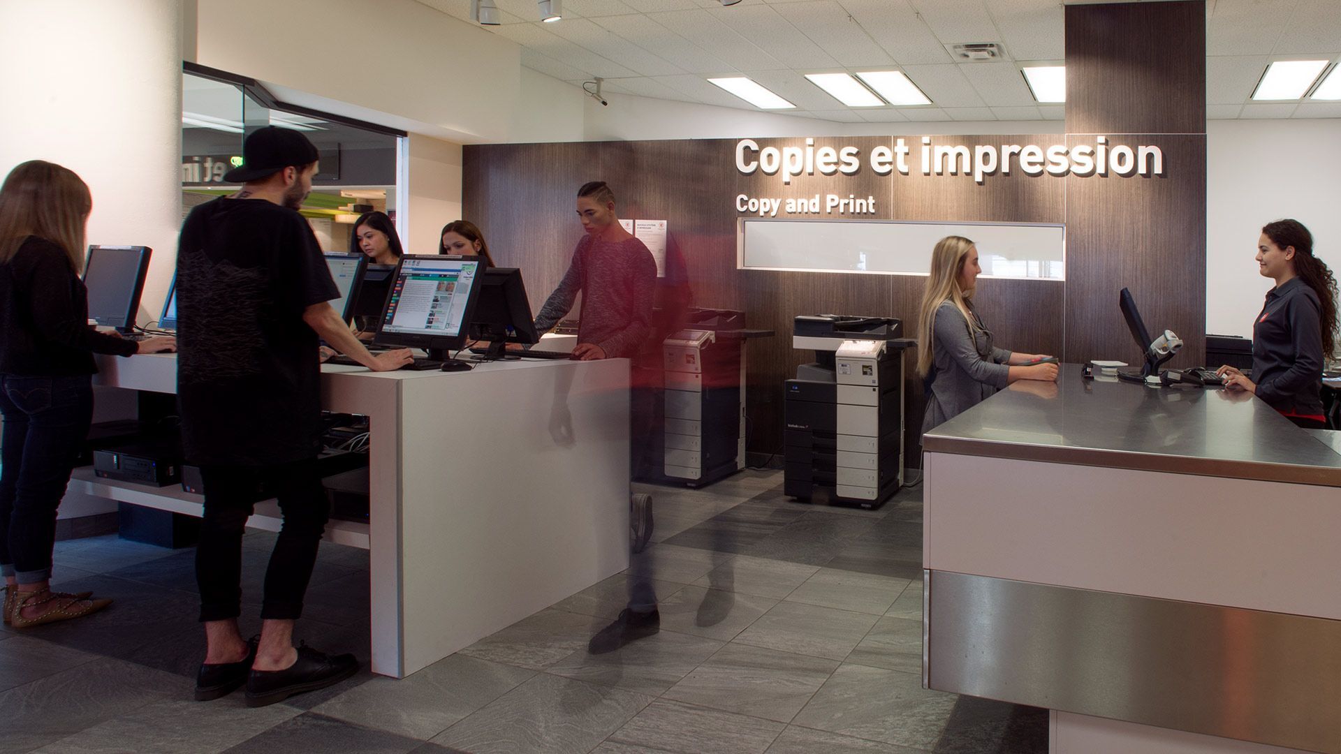 Clients et employés dans un centre de services d'impression moderne avec ordinateurs et photocopieuses.