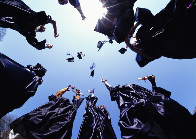 Des diplômés jetant leurs chapeaux en l'air, capturés depuis un angle bas contre un ciel dégagé, transmettant un sentiment de réussite et de joie.