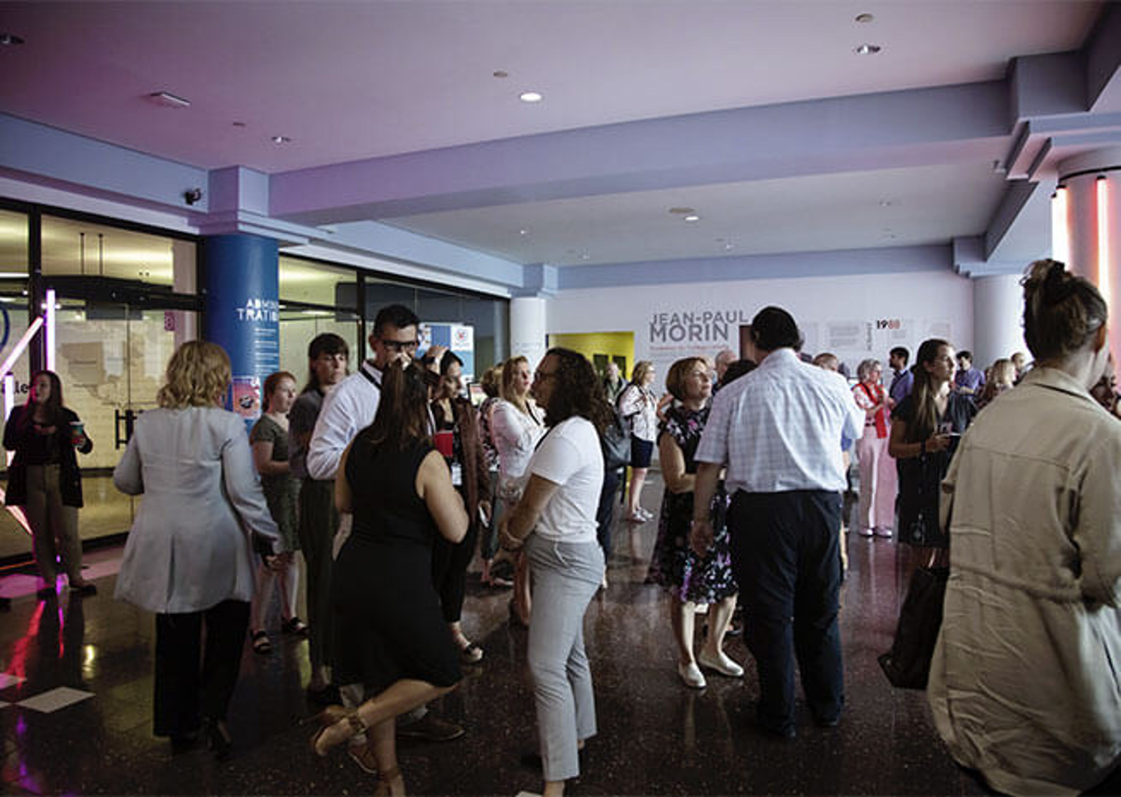 Attendees at a conference mingle during a break in the lobby area, engaging in professional networking.